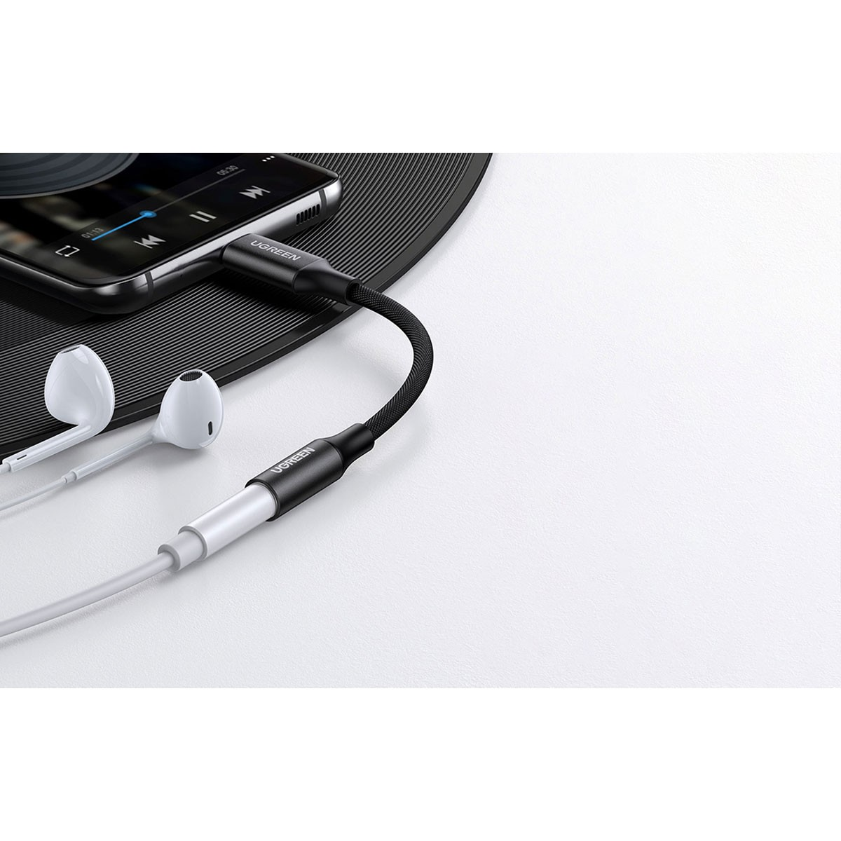 Czarno-biały adapter audio podłączony do telefonu i słuchawek. Znajduje się na czarnej płycie winylowej.