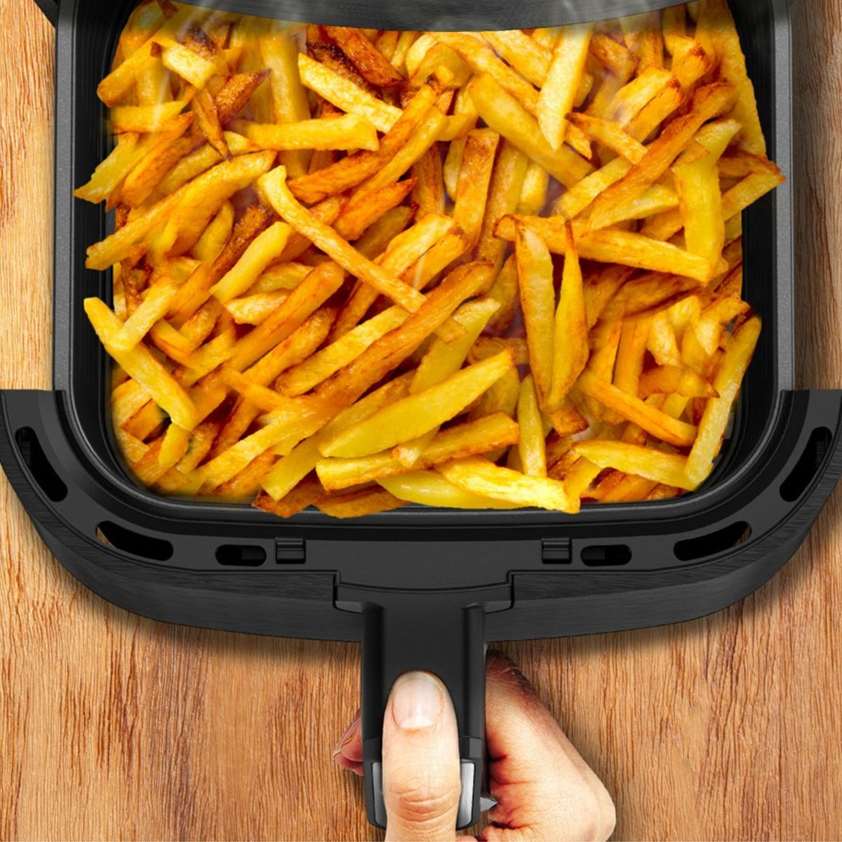 Zbliżenie kosza frytkownicy powietrznej wypełnionego złocistobrązowymi frytkami, leżącego na drewnianej powierzchni.