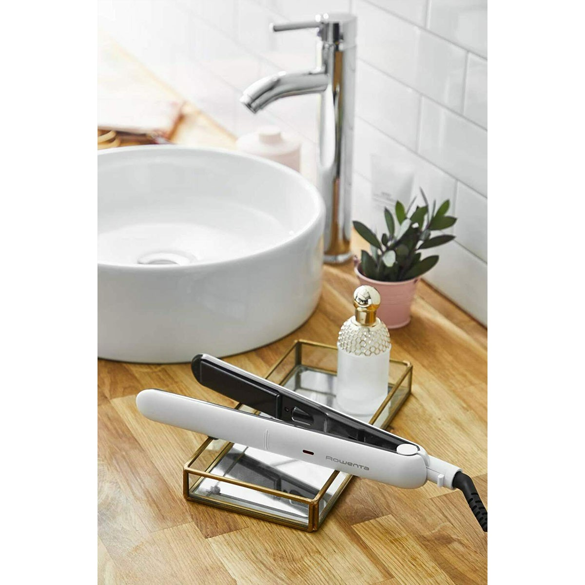 Escena de baño con lavabo blanco, secador y plancha en mostrador de madera.