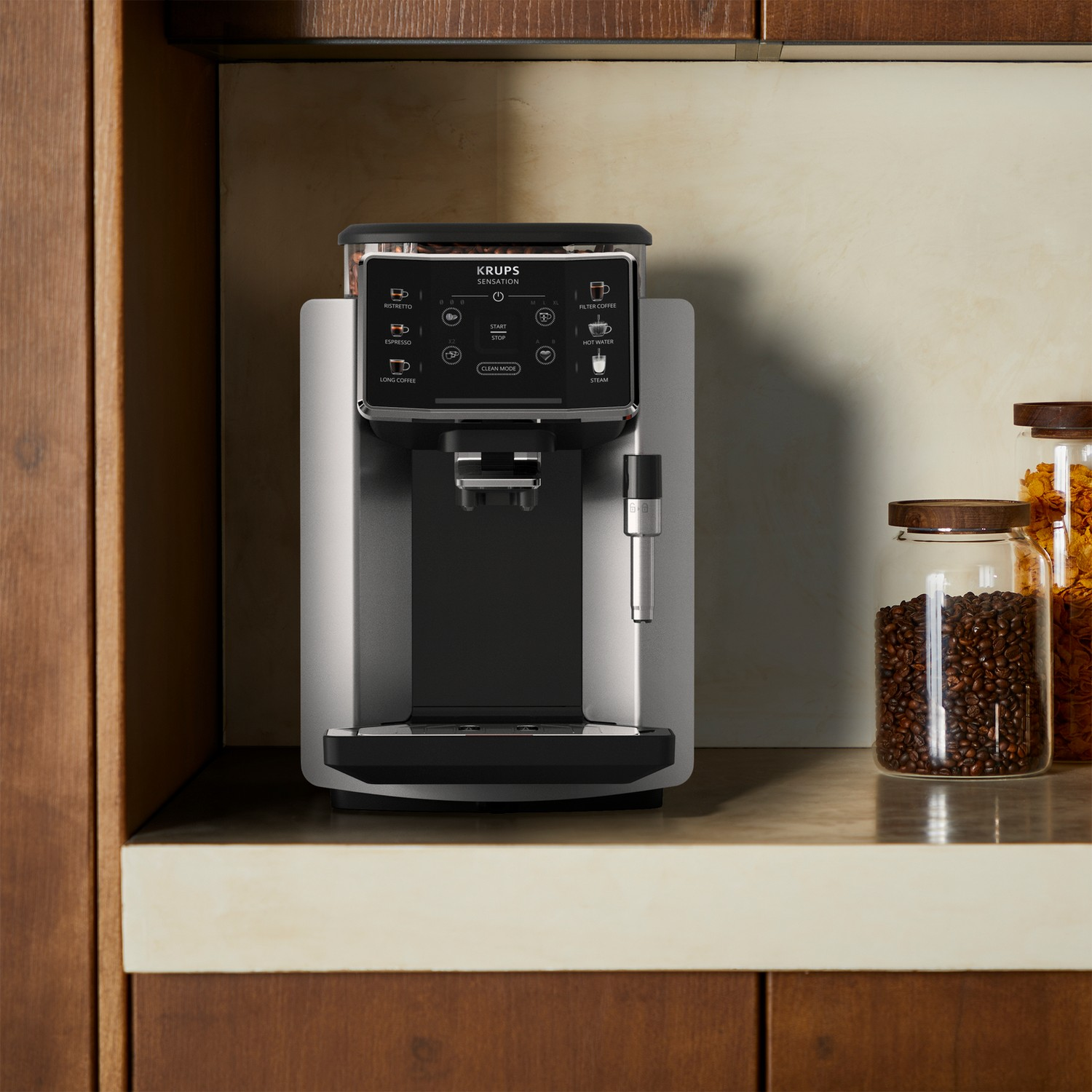 Srebrno-czarny ekspres do kawy Krups Sensation ze słoikami ziaren kawy, na drewnianej powierzchni.
