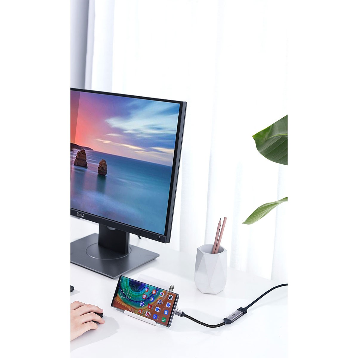 Telefon podłączony do monitora kablem na białym biurku. Monitor wyświetla krajobraz.