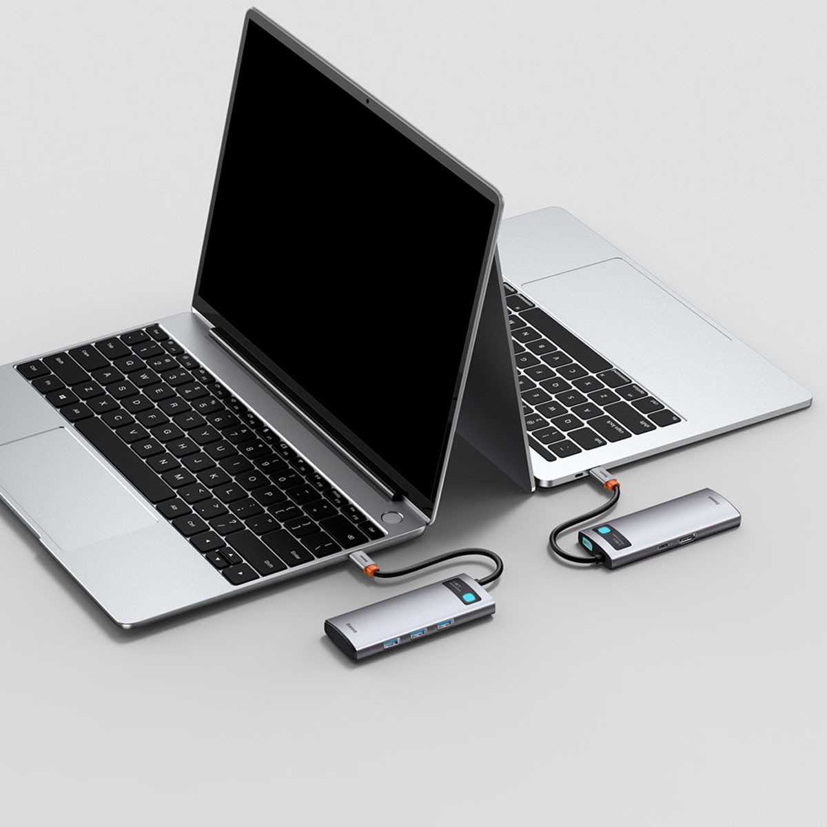 Zwei Laptops, die mit silbernen USB-Hubs verbunden sind, auf einer hellen Oberfläche. Kabel sichtbar.