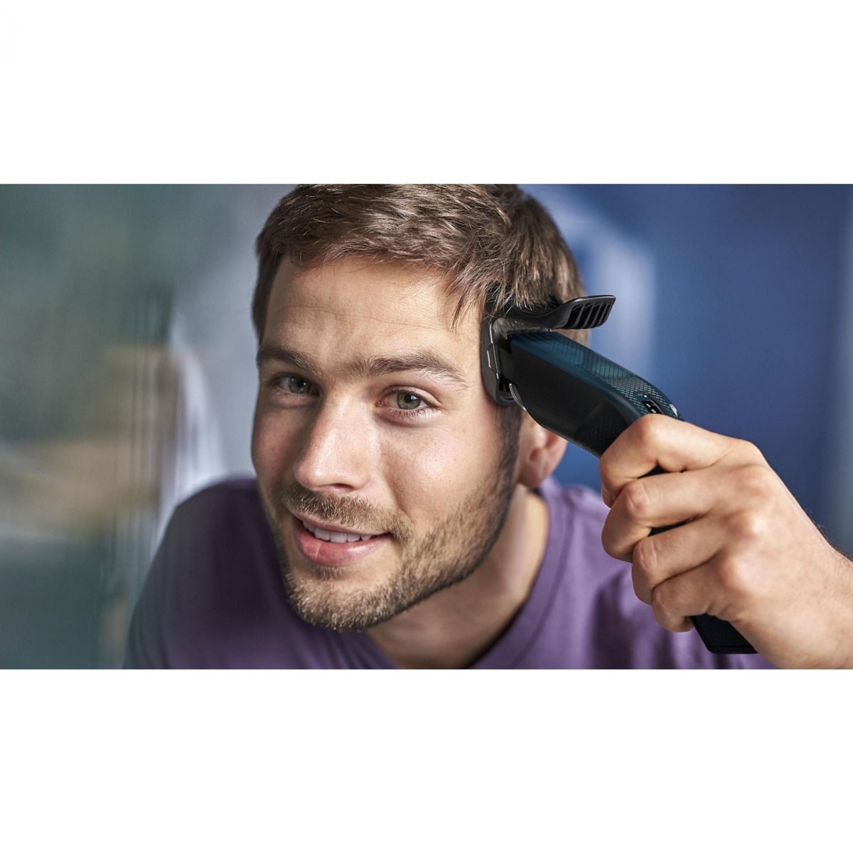 Ein Mann schneidet sich mit einem schwarzen Haarschneider die Haare und lächelt.