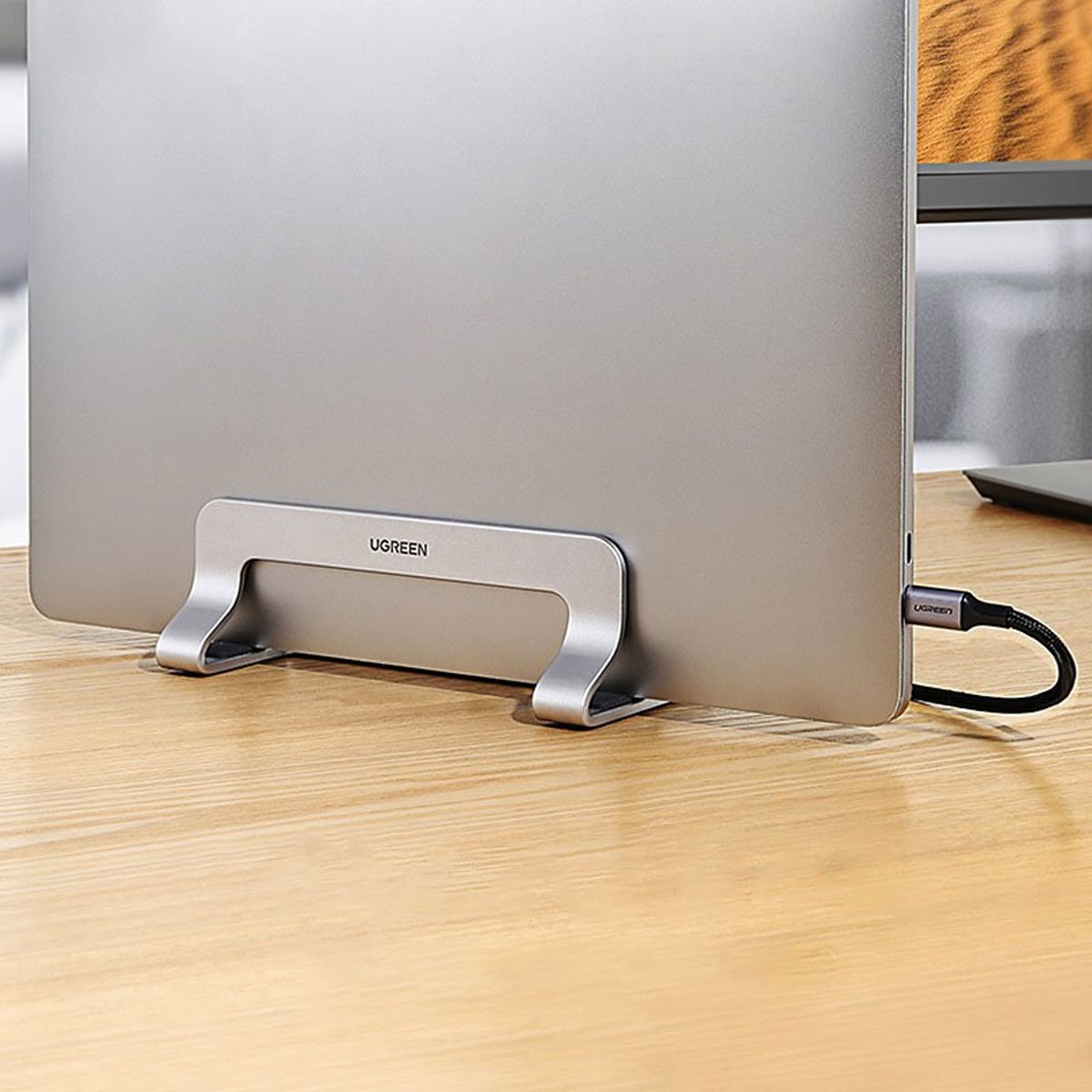 Laptop auf einem silbernen Ständer, angeschlossen an ein USB-C-Kabel, auf einem Holzschreibtisch.