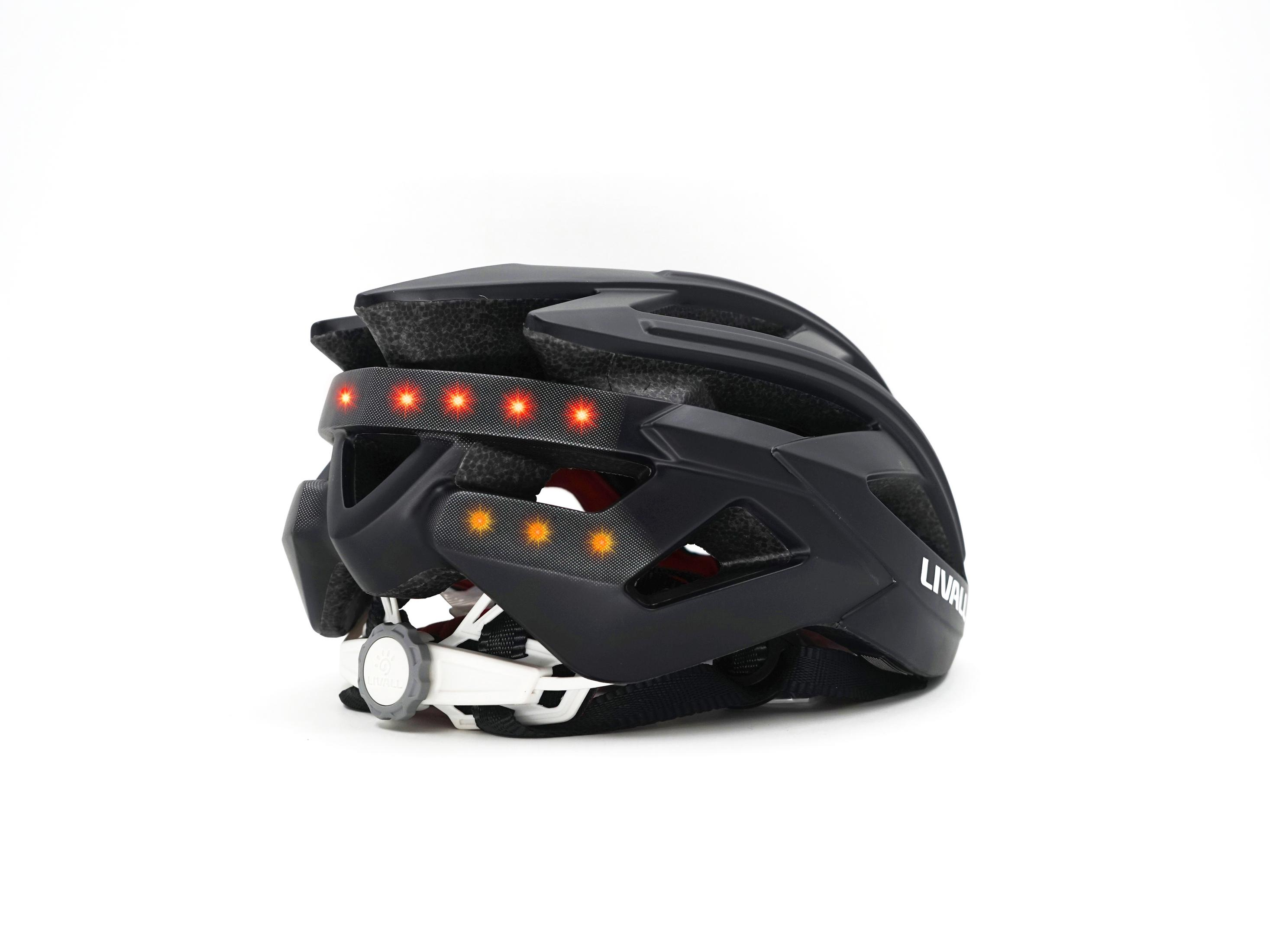 Schwarzer Fahrradhelm mit roten Lichtern hinten. Weißer Hintergrund.