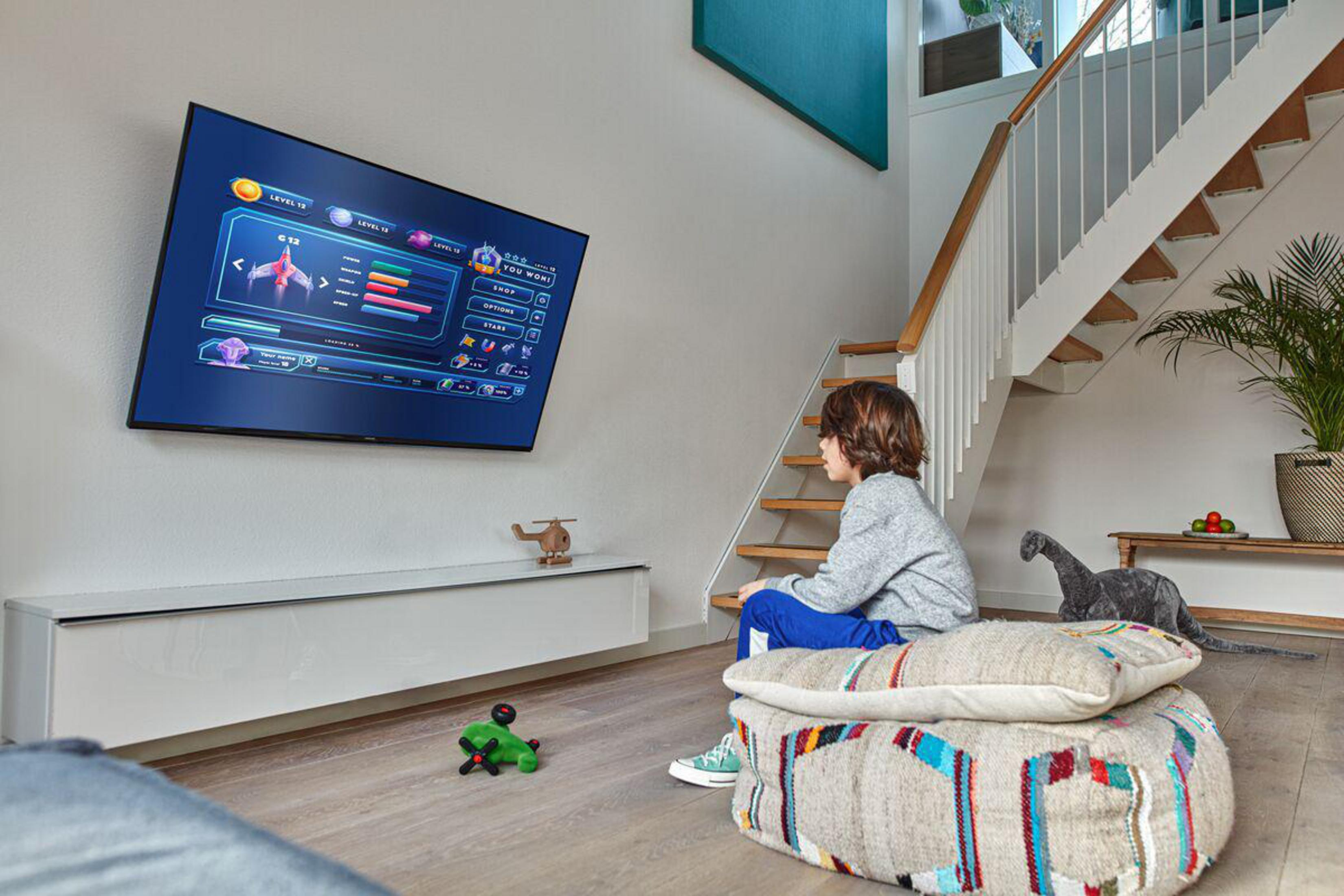 Chłopiec siedzący na poduszce podłogowej ogląda telewizor zamontowany na ścianie.