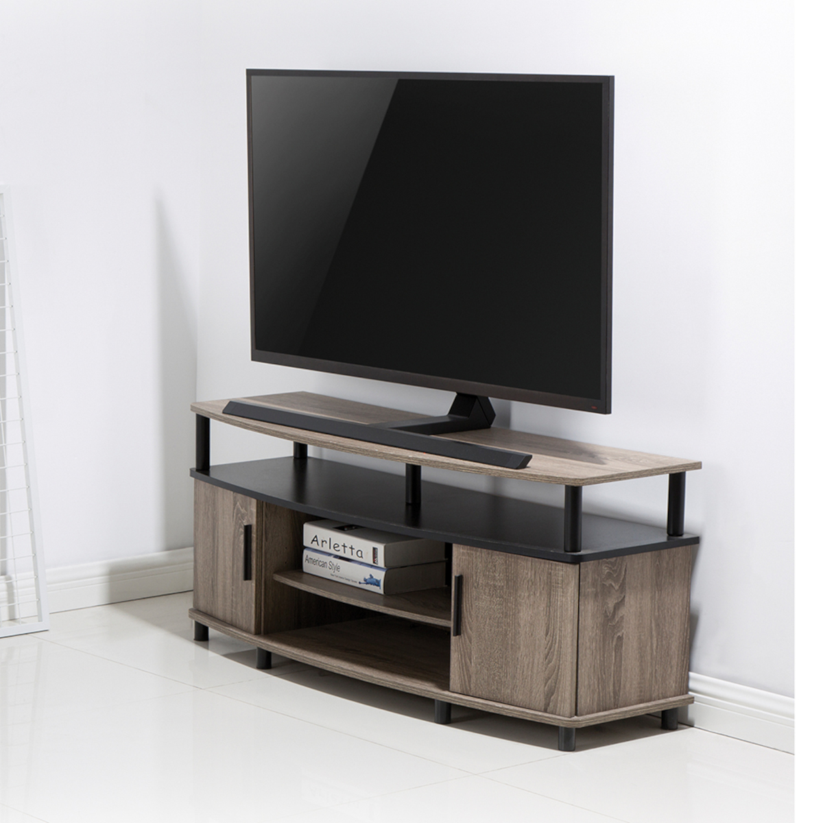 Ein TV-Ständer aus Holz mit einem Fernseher oben drauf. Er hat Türen und Regale, vor einer weißen Wand.
