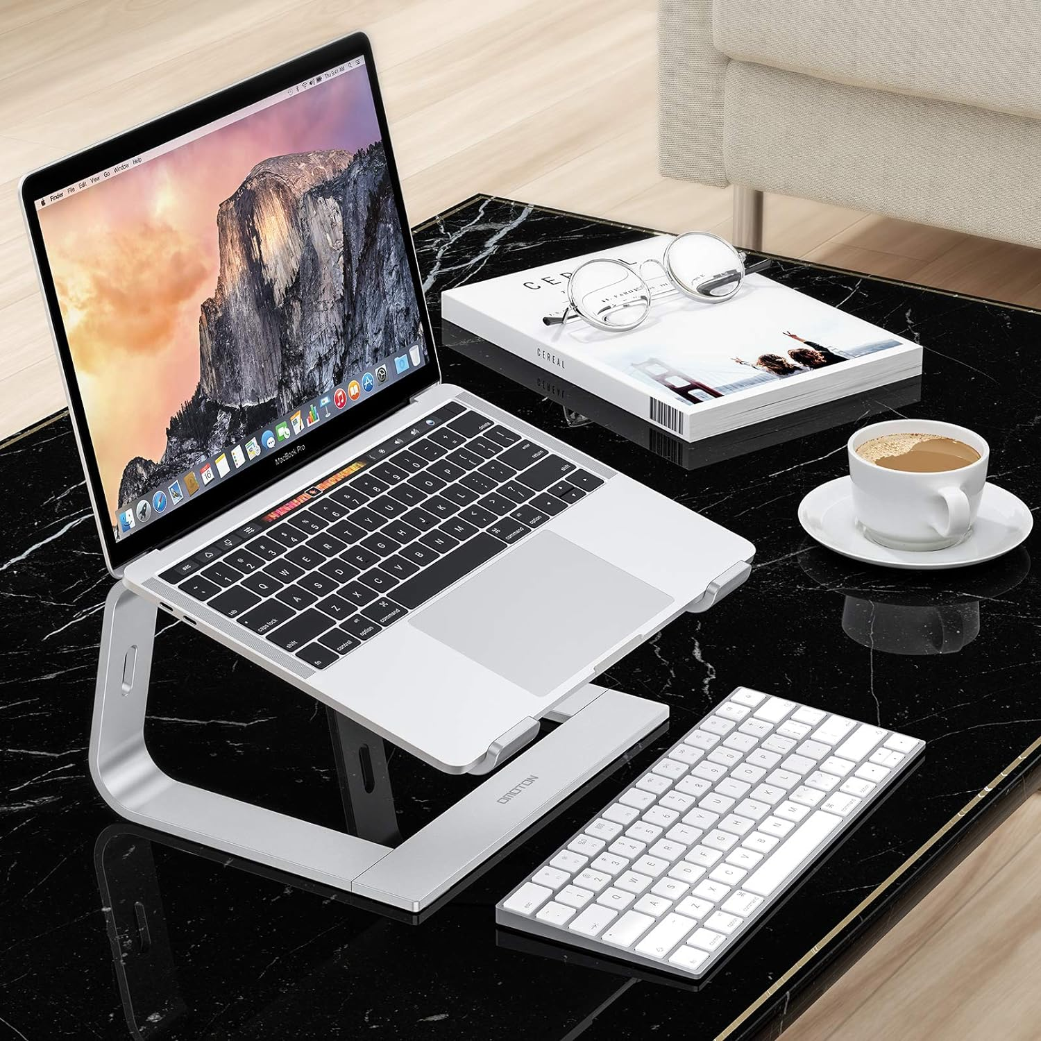 Laptop auf einem Ständer mit Tastatur und Kaffeetasse. Der Hintergrund ist schwarzer Marmor.