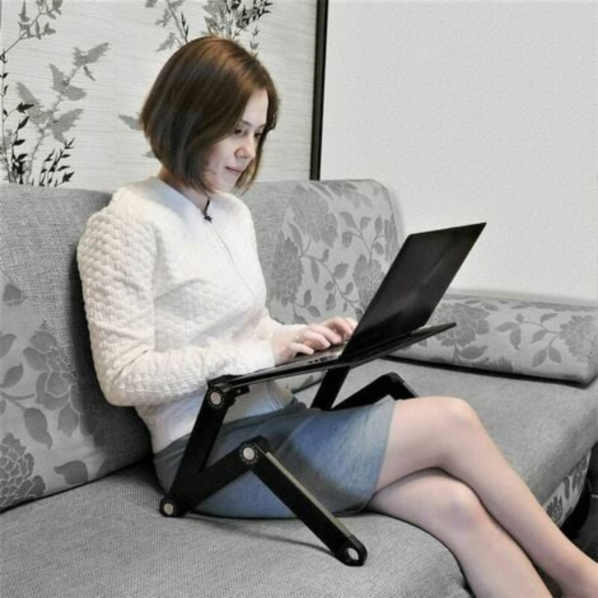 Frau benutzt Laptop auf einem schwarzen Laptopständer auf dem Sofa.