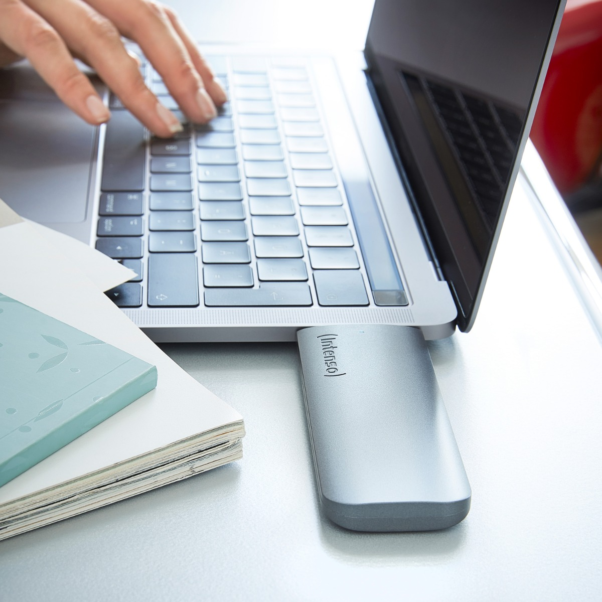 Eine Person tippt auf einem Laptop, an dem eine externe silberne Festplatte angeschlossen ist.
