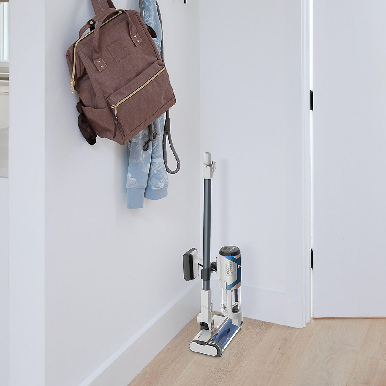 Ein Staubsauger steht an einer Wand neben einem Rucksack und einem Mantel.