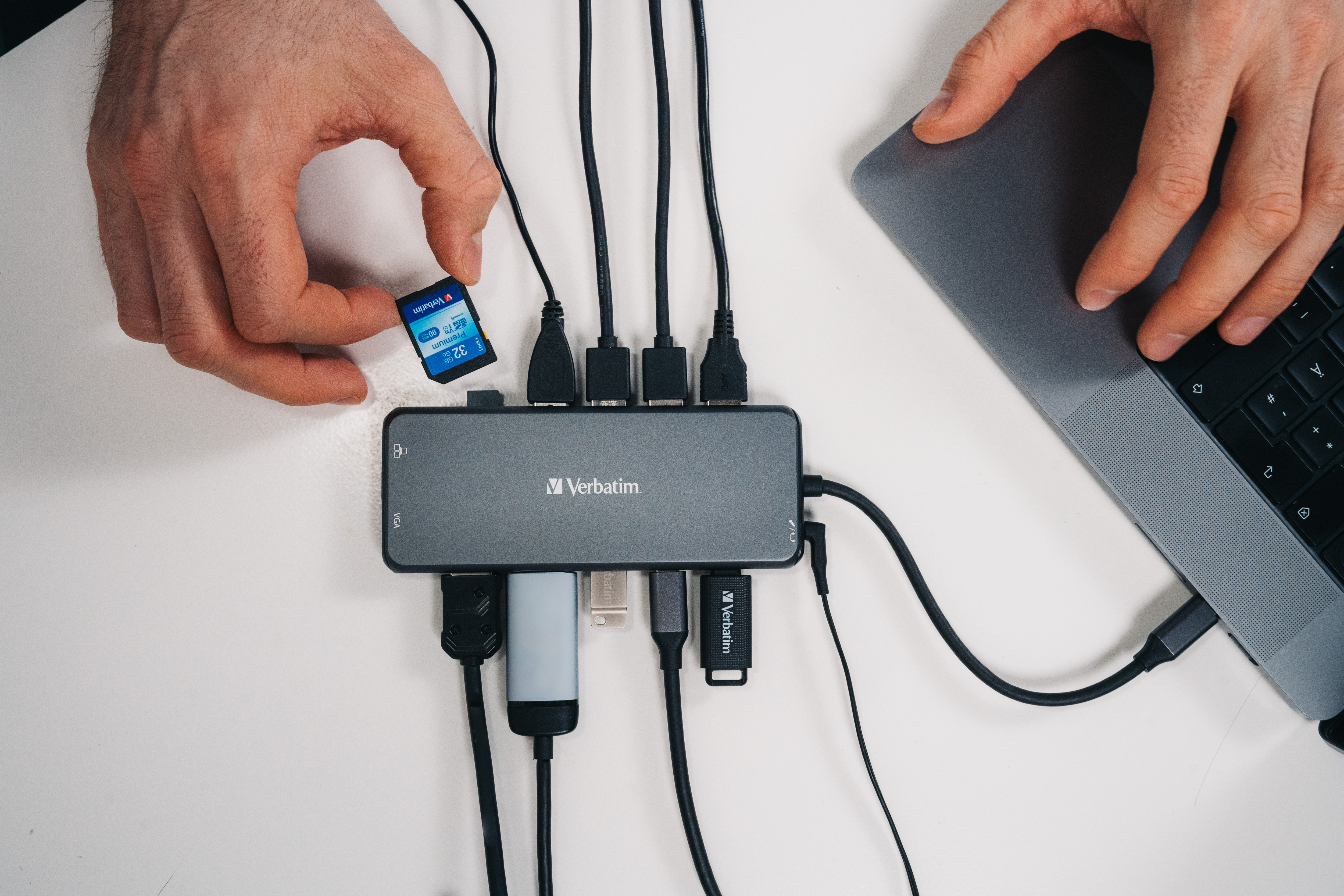 Mani con scheda SD, collegata a hub con cavi USB e laptop.
