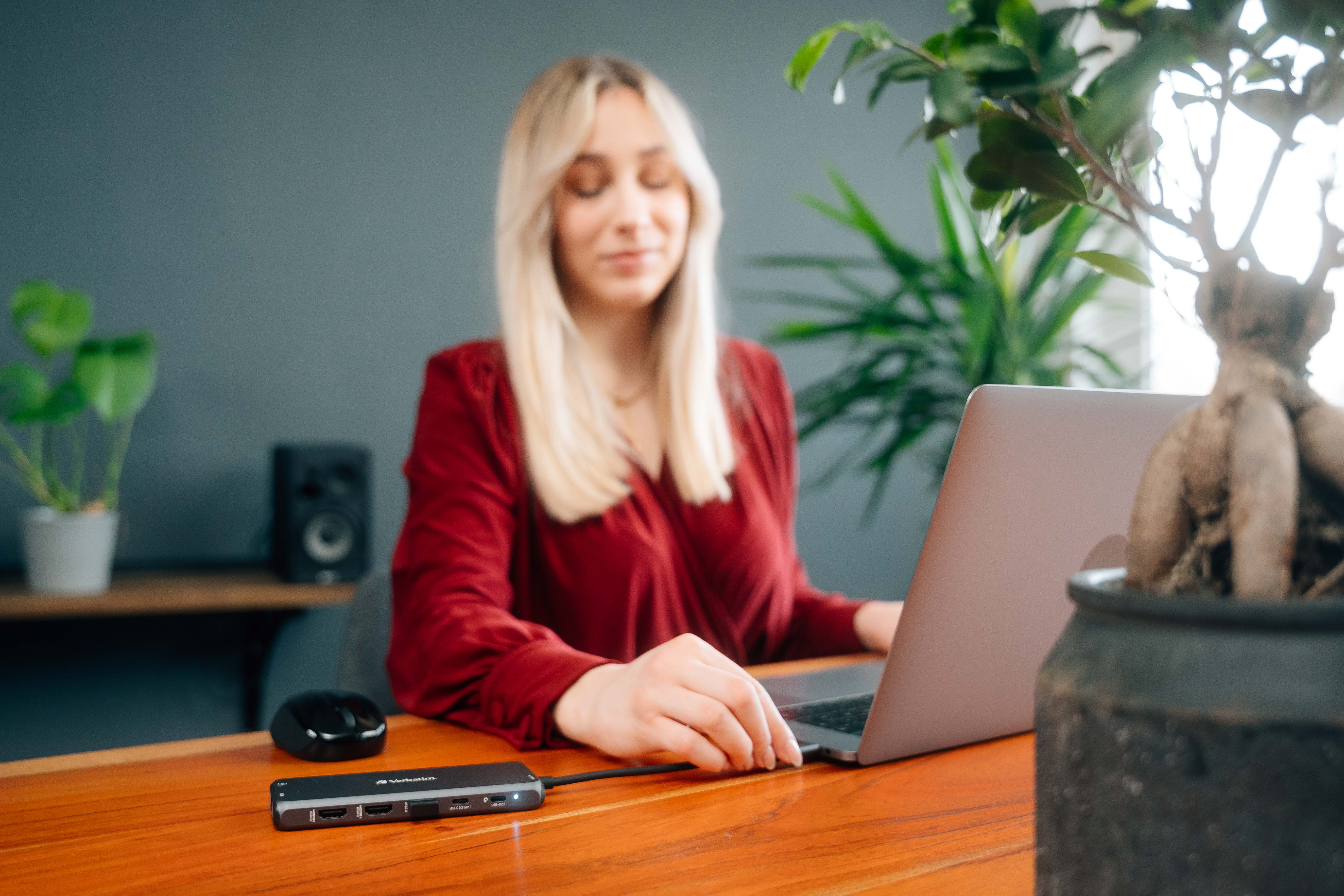 Una donna usa un laptop a una scrivania, con un hub e chiavette USB. Visibili una pianta e un altoparlante.