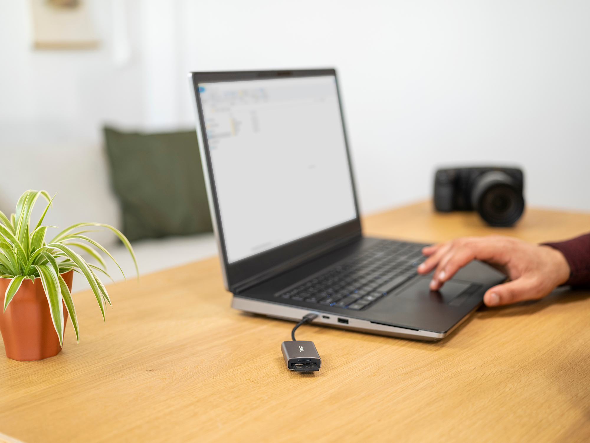 Un portátil conectado a un concentrador USB y una cámara en la mesa. Planta a la izquierda.