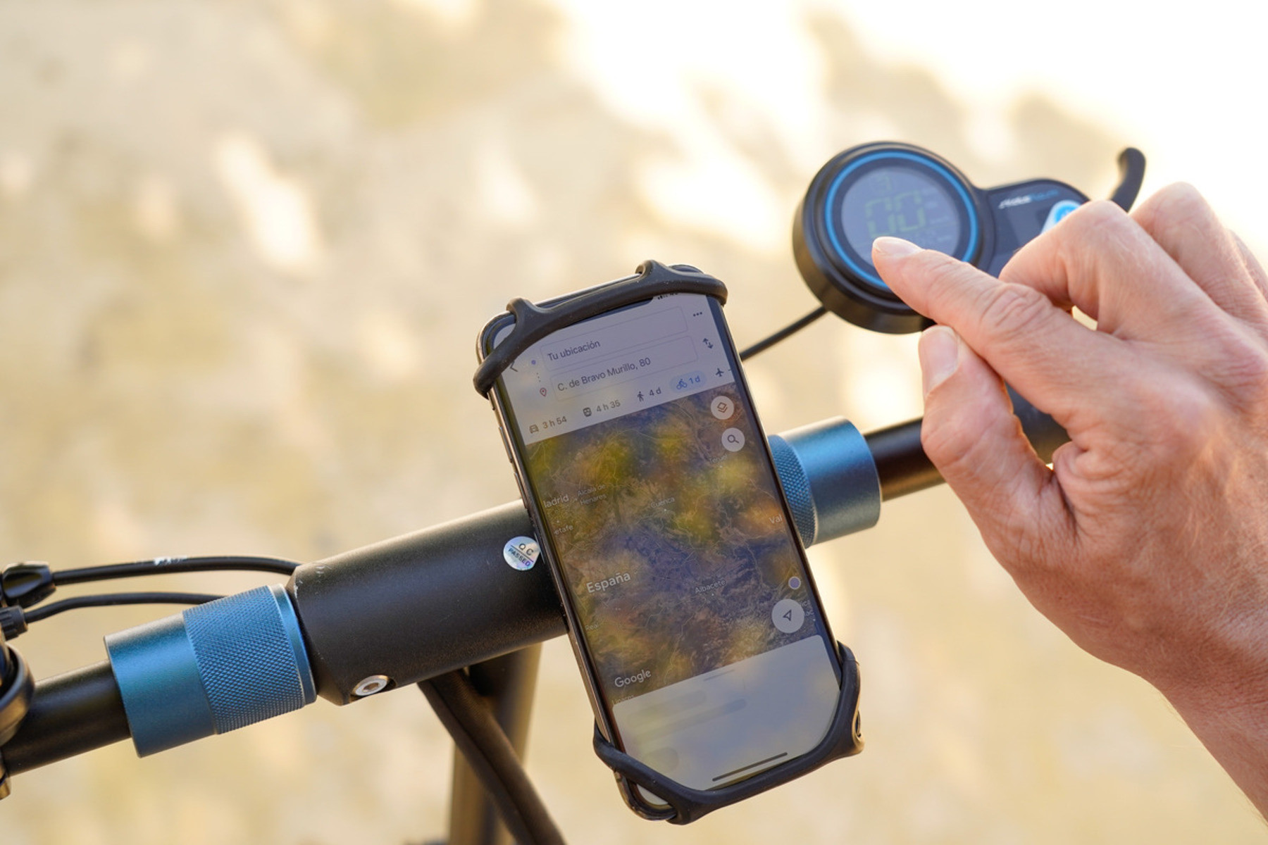 La mano de una persona en el manillar de un scooter. Un teléfono muestra un mapa. La pantalla del scooter muestra la velocidad.