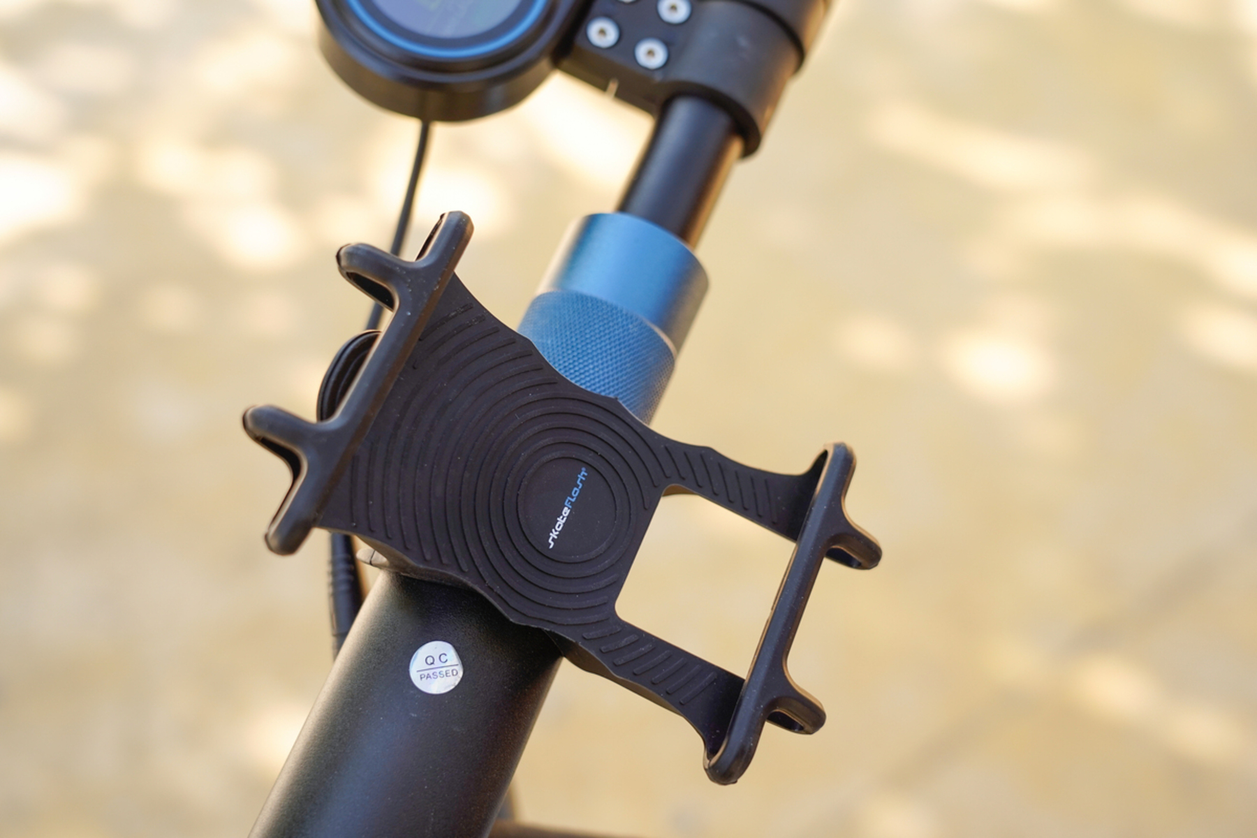 Un soporte para teléfono sujeto al manillar de un scooter. Es negro y tiene texto.