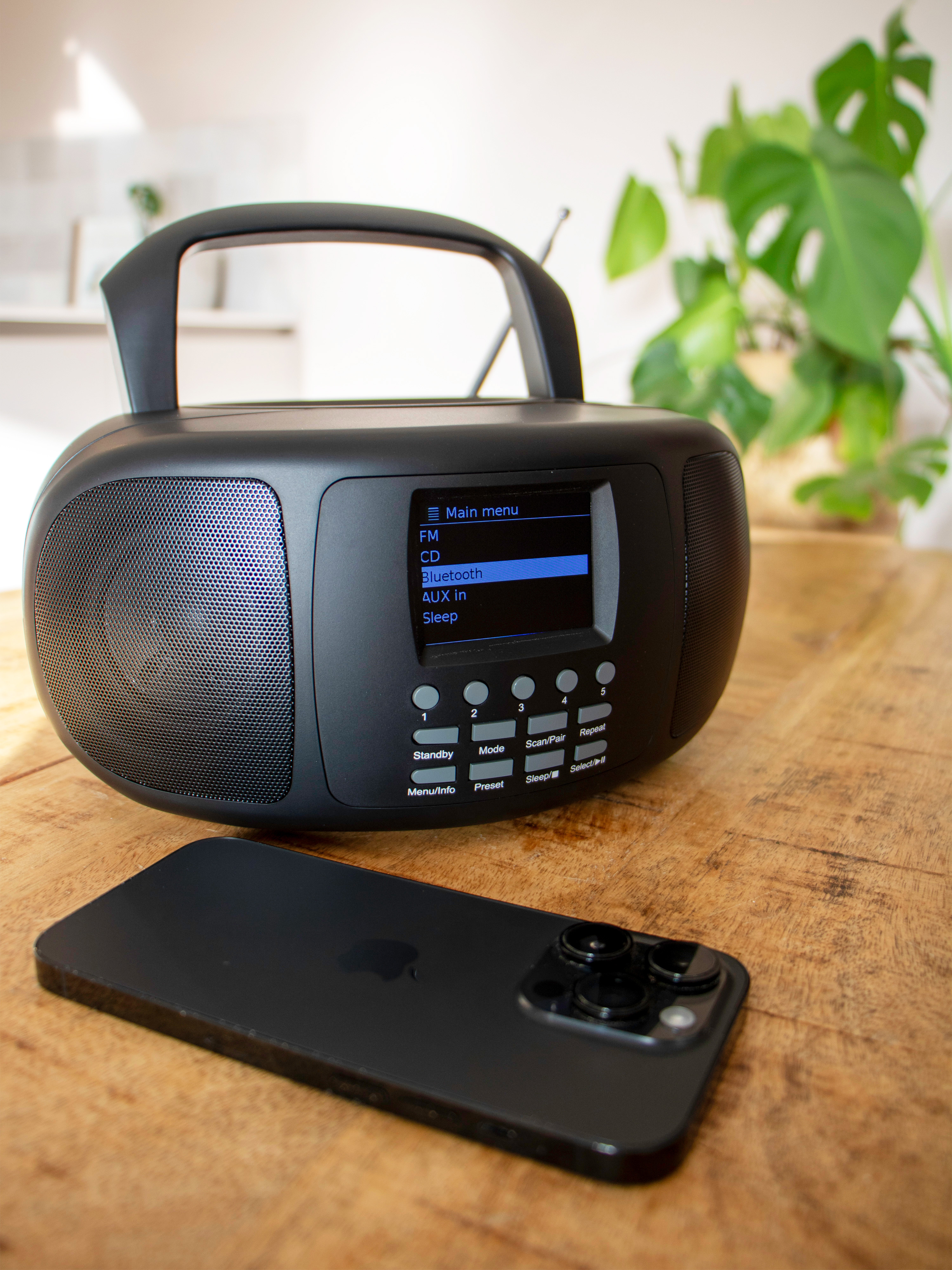 Czarne radio z telefonem na drewnianym stole. Radio ma ekran wyświetlający menu.