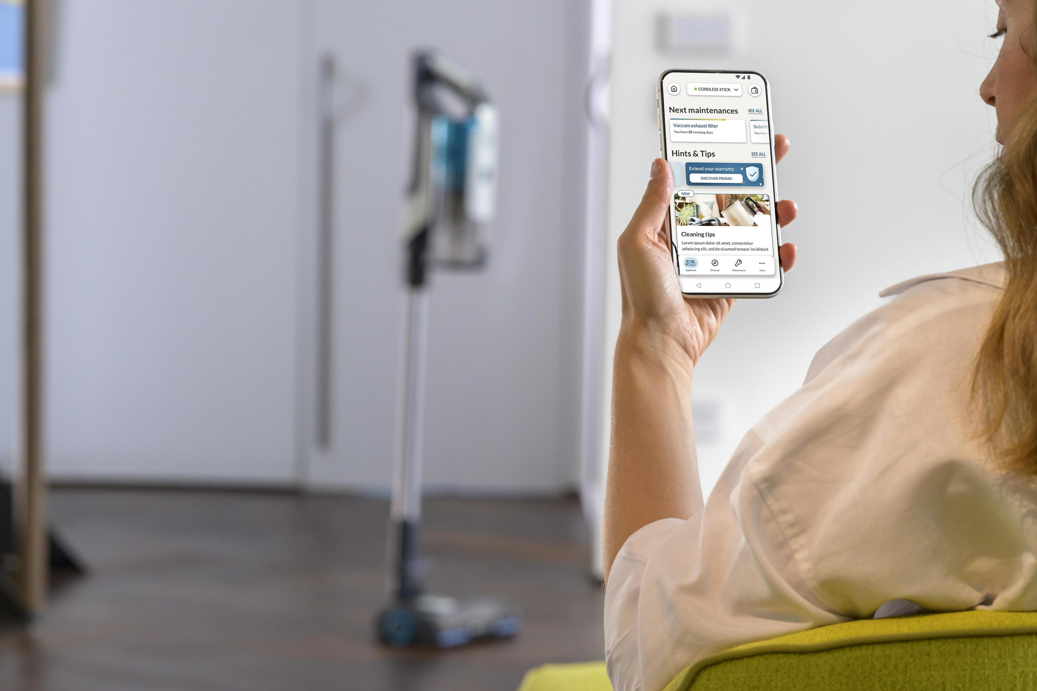 Kobieta trzymająca smartfona z odkurzaczem w tle, telefon wyświetla wskazówki dotyczące konserwacji.
