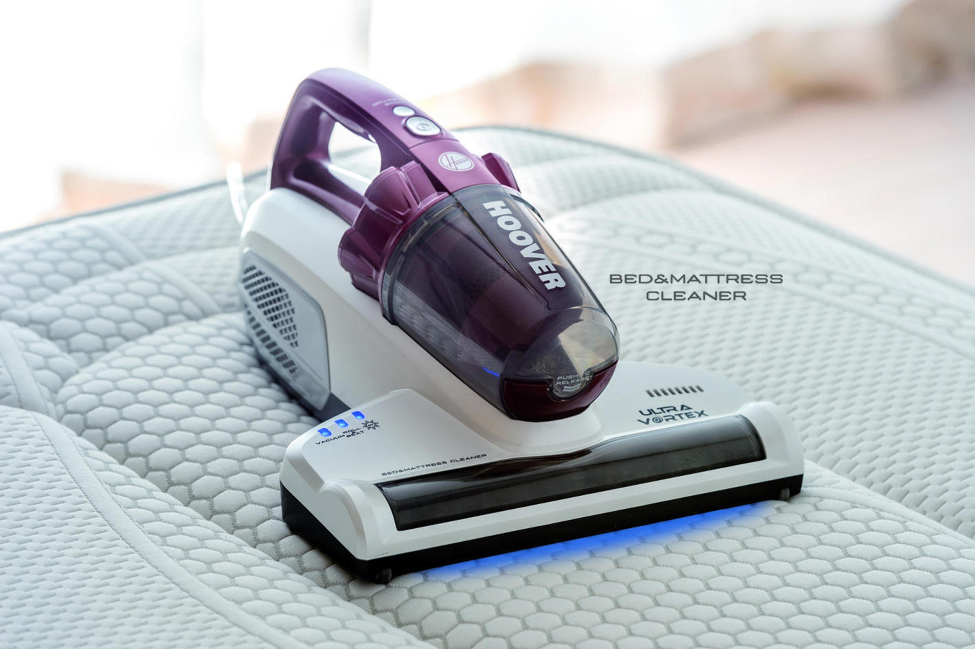 Una aspiradora Hoover blanca y morada sobre un colchón con manchas, con texto que indica su uso.