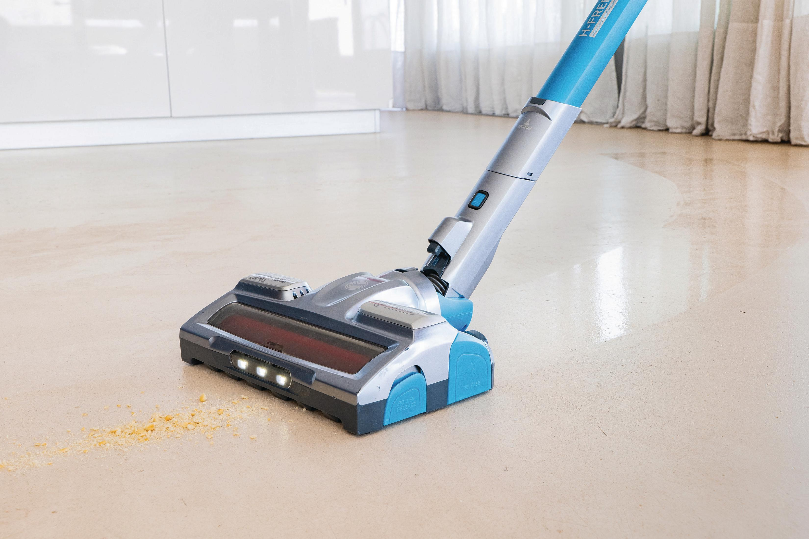 Niebiesko-srebrny odkurzacz bezprzewodowy na jasnej podłodze, czyszczący kurz.