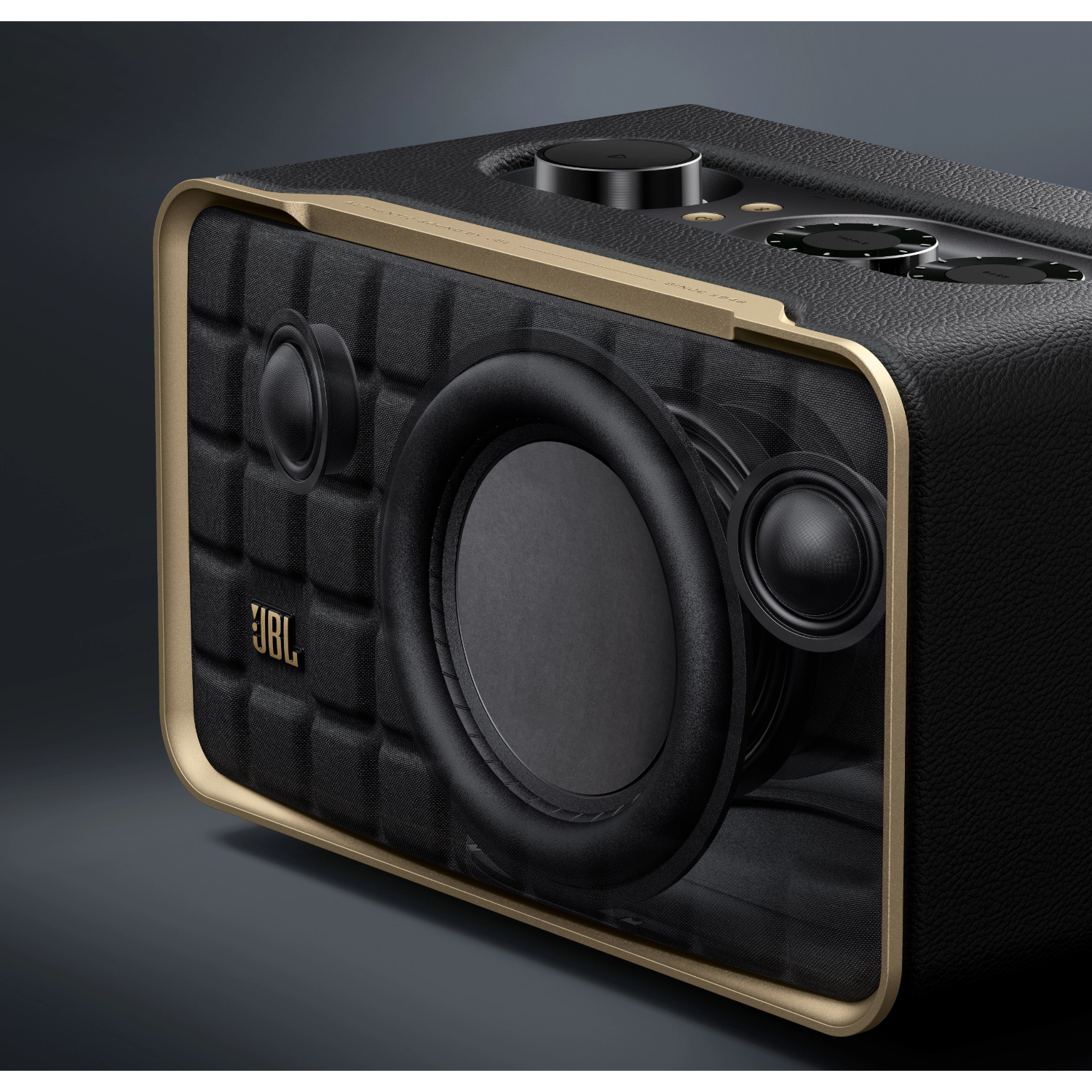 Zbliżenie czarnego głośnika JBL ze złotą ramą. Głośnik ma pikowany skórzany przód.