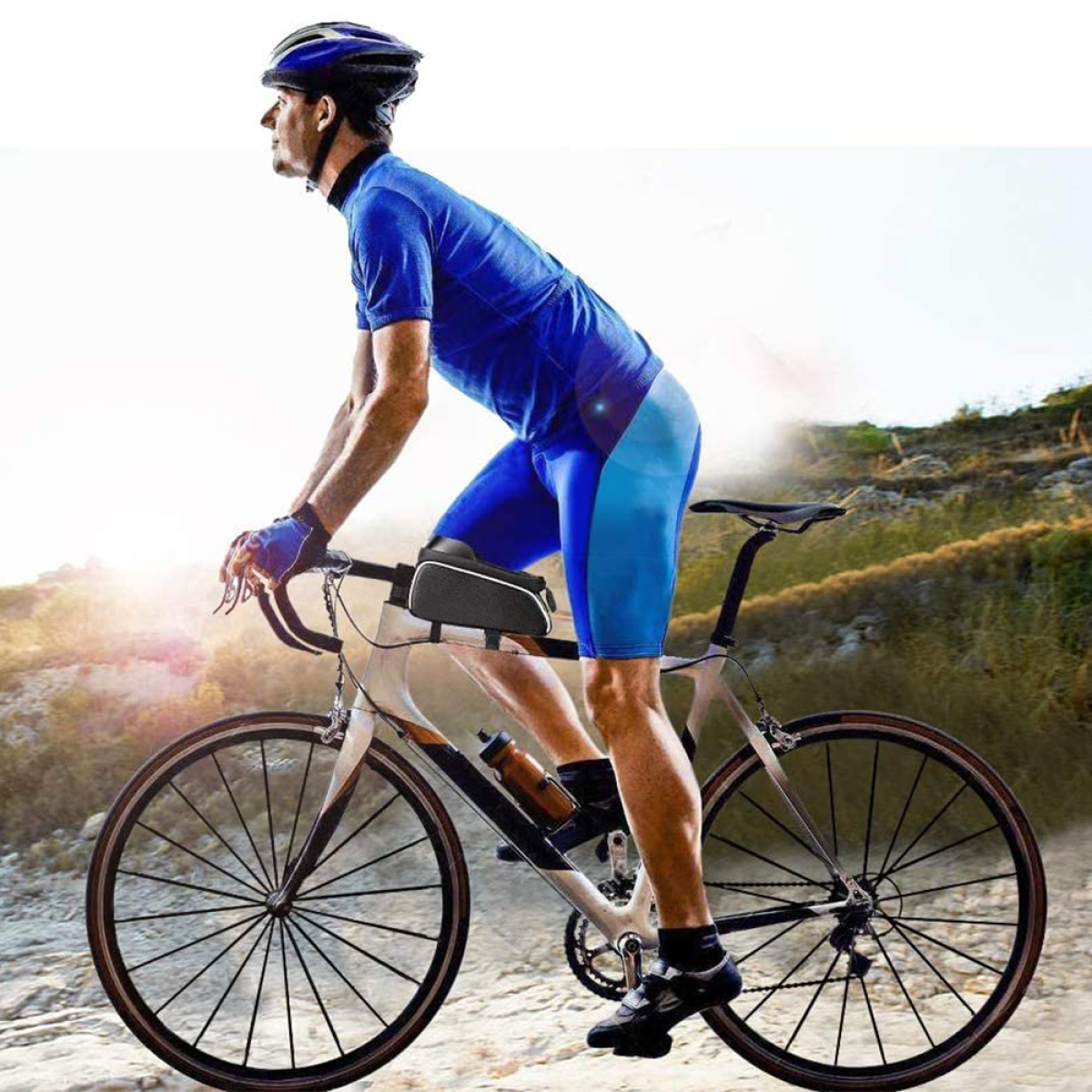 Radfahrer fährt auf einer Schotterstraße mit blauem Trikot und Hose. Sonniger Tag.