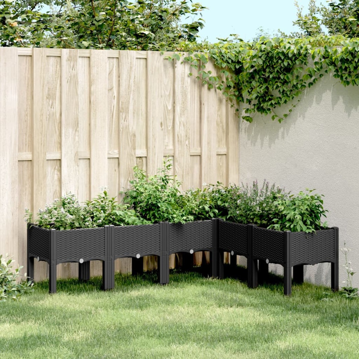Schwarze Hochbeete in einem Garten mit Holzzaun und Grün.