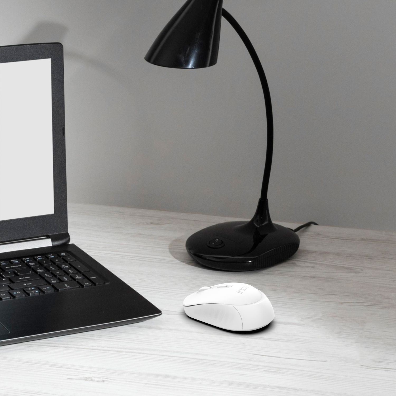 Eine weiße Maus und eine schwarze Lampe auf einem Schreibtisch, mit einem Laptop im Hintergrund.