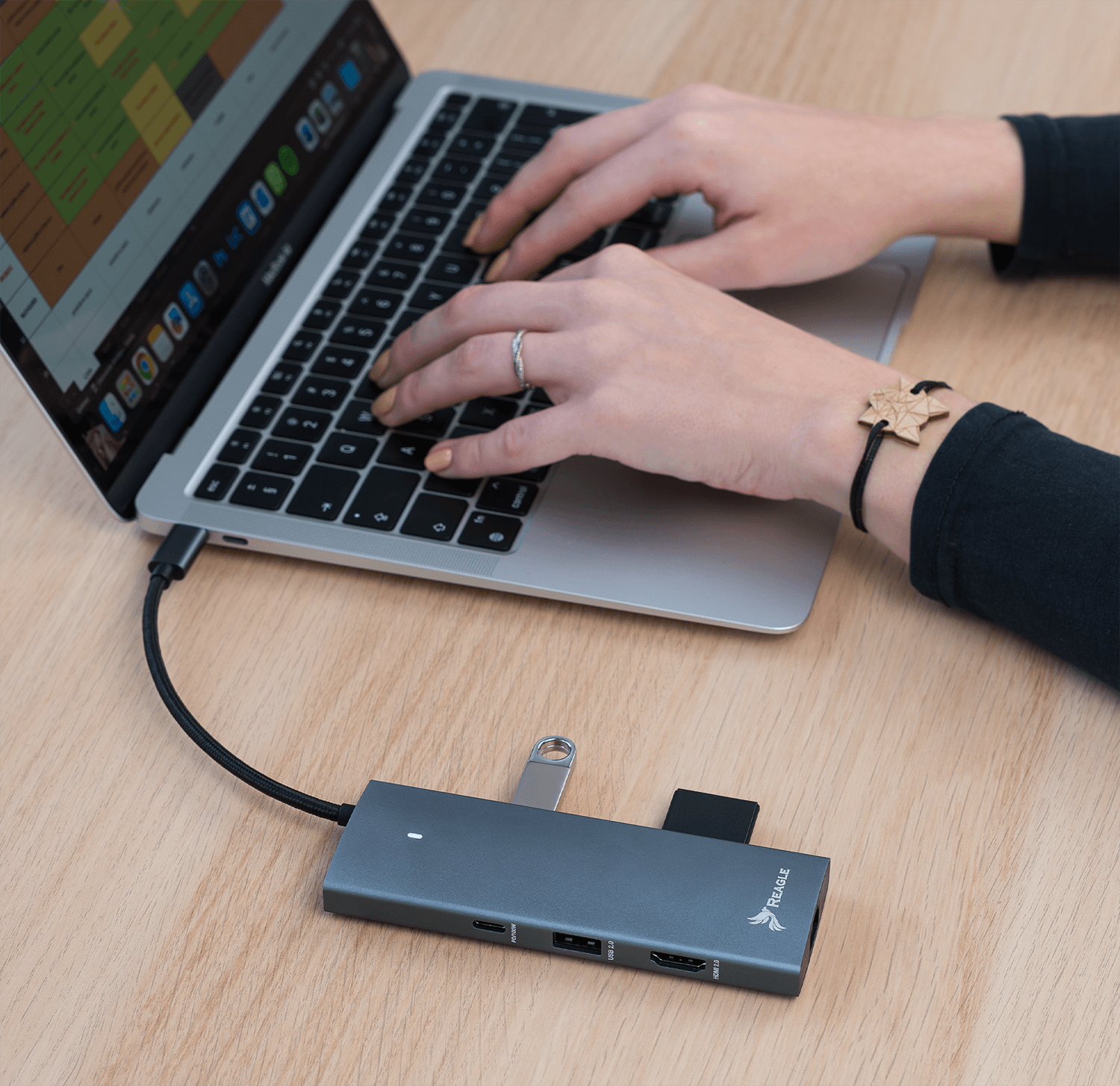 Osoba pisząca na laptopie podłączonym do huba. Hub z portami USB, SD i HDMI.