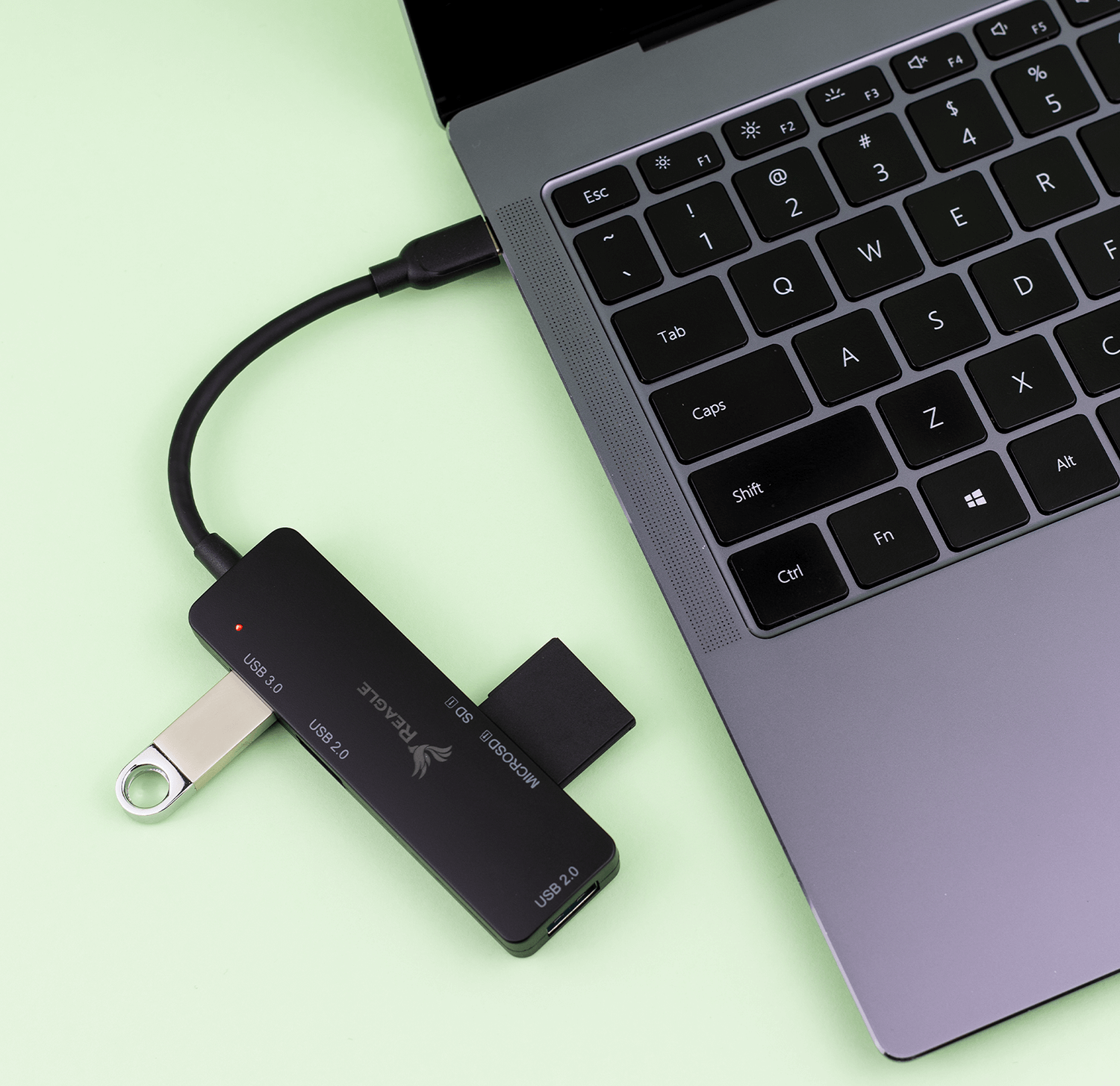 Ein schwarzer USB-Hub mit USB-Laufwerk und SD-Karte, verbunden mit einem Laptop auf grüner Oberfläche.