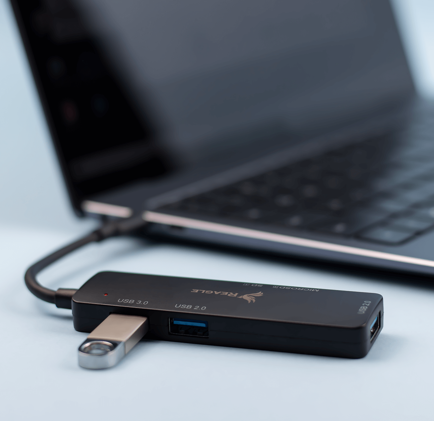 Ein schwarzer USB-Hub, der mit einem Laptop verbunden ist. Er hat einen silbernen USB-Stick und ein Logo.