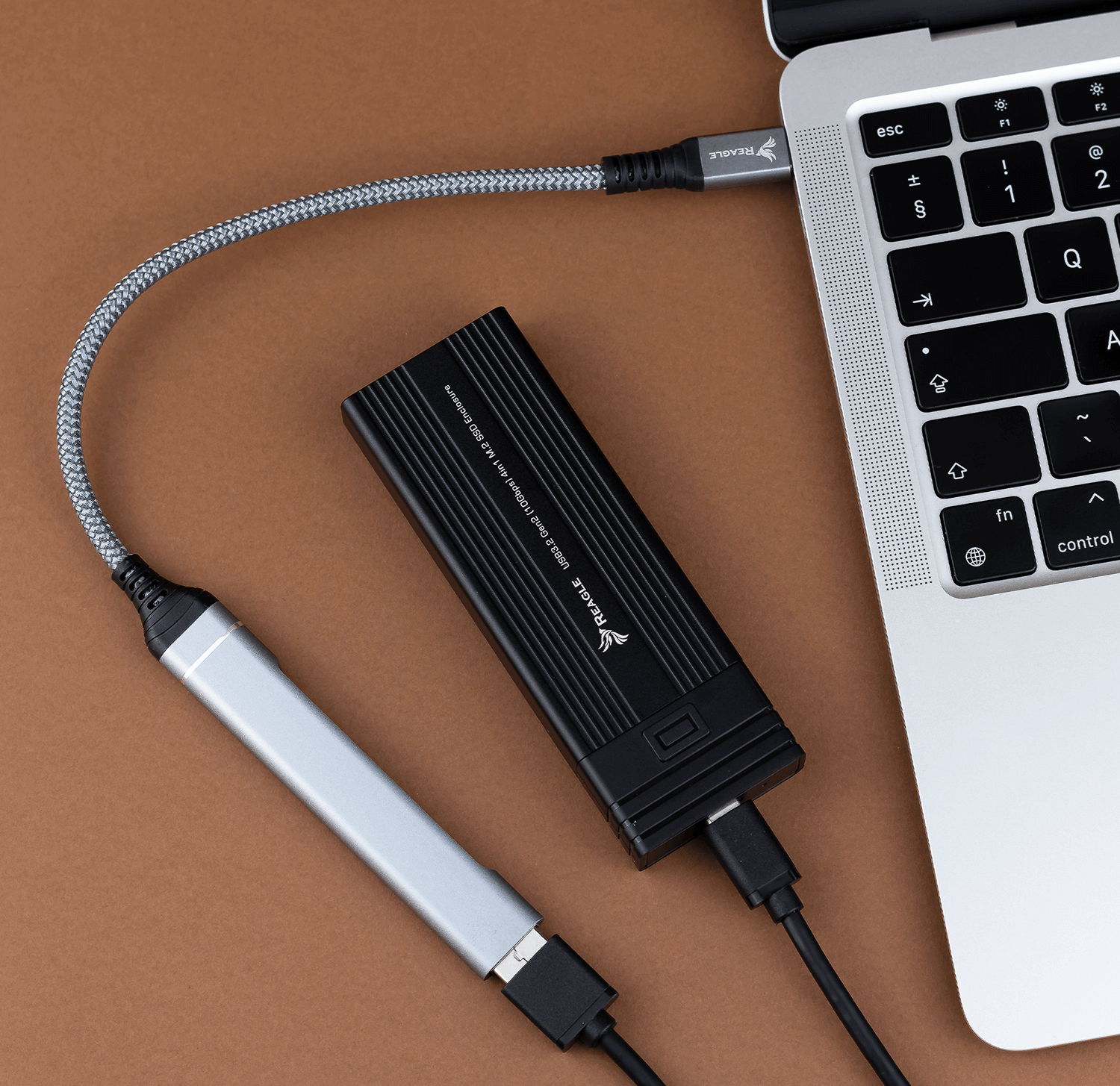 Czarny zewnętrzny dysk twardy podłączony do laptopa za pomocą szarego kabla. Laptop na brązowej powierzchni.