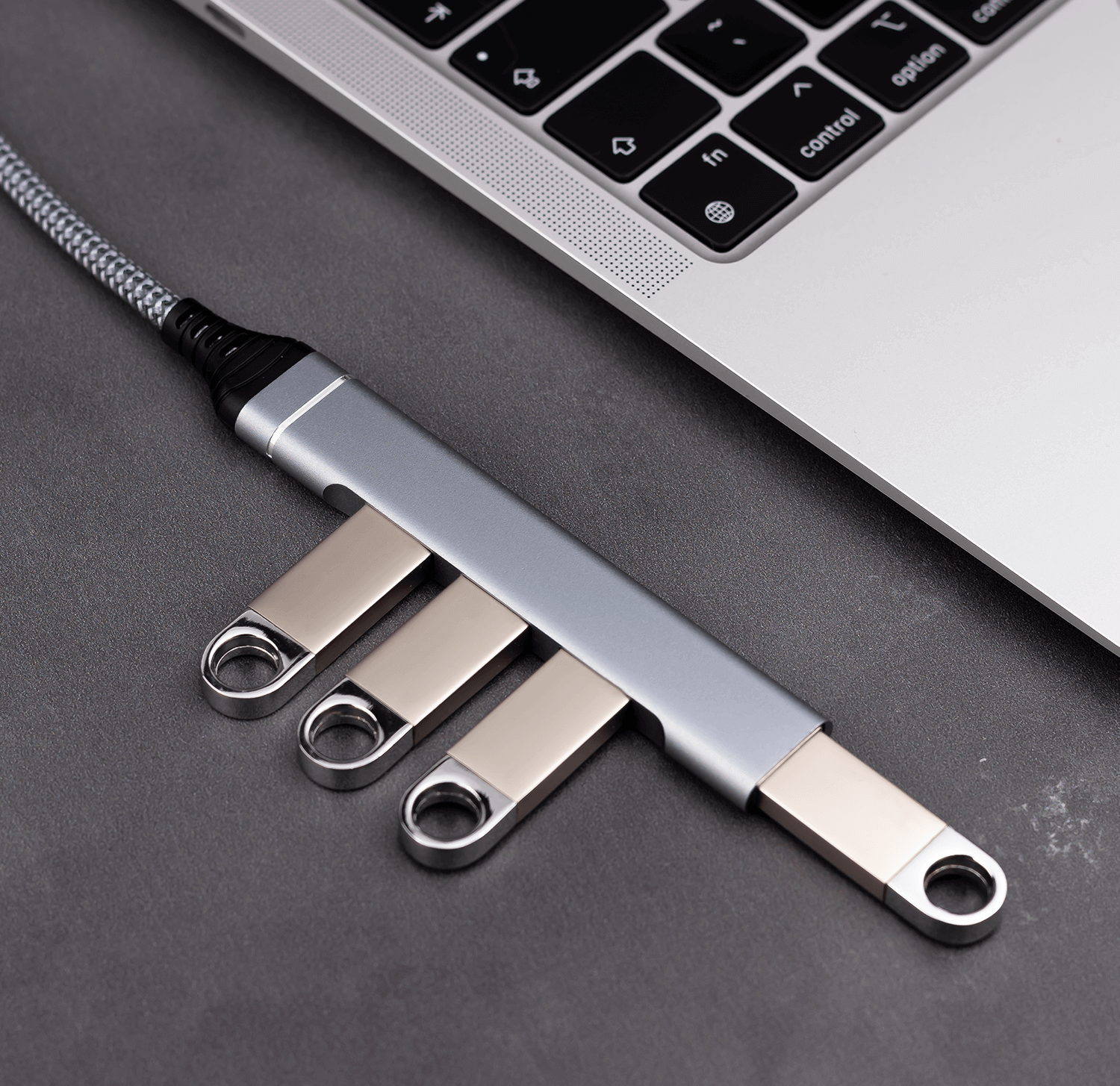 Hub USB-C, trzy srebrne pendrive'y i laptop są widoczne.