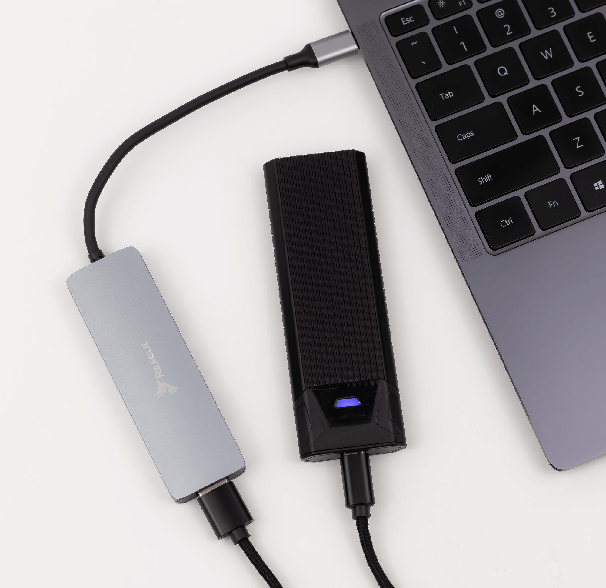 Laptop, verbunden mit einem silbernen USB-Hub und einer schwarzen externen Festplatte, auf Weiß.