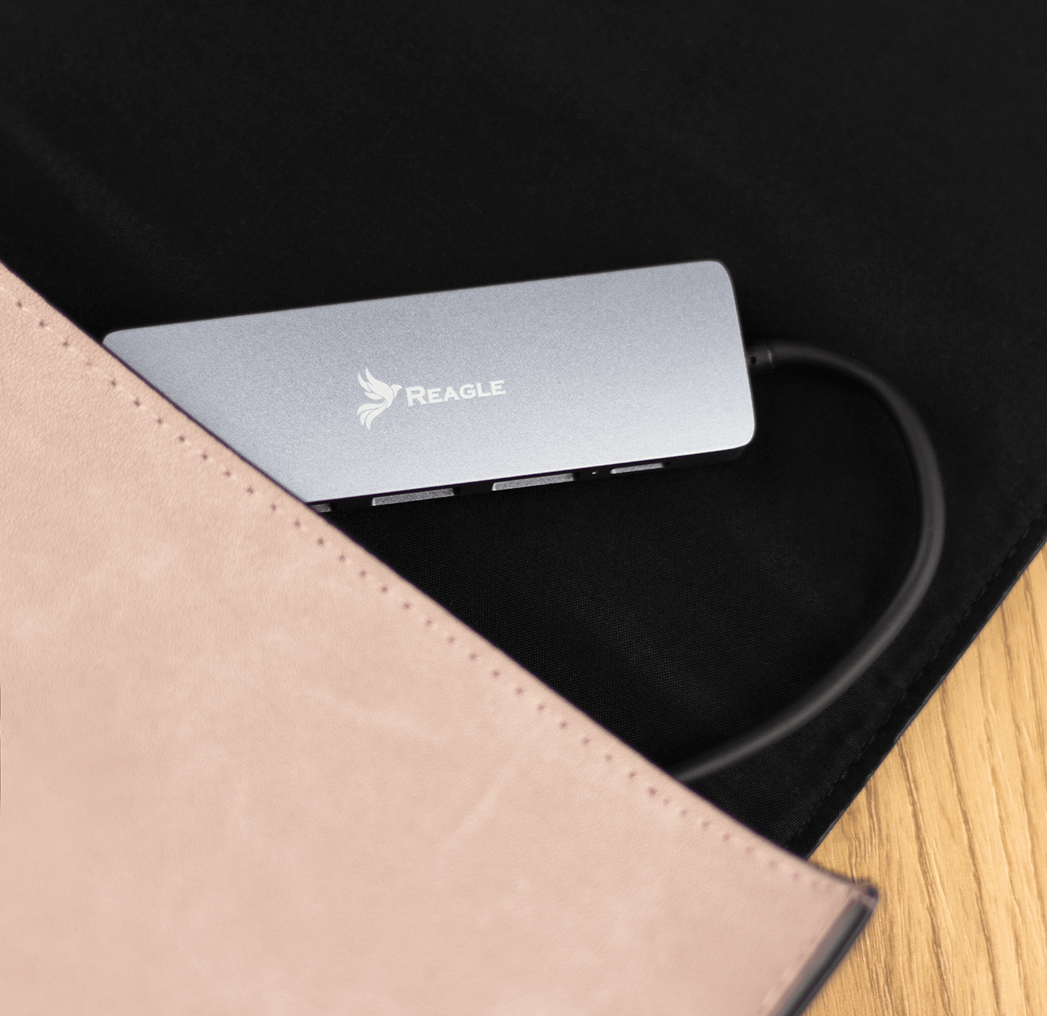 Ein silberner Reagle USB-Hub mit schwarzem Kabel und einem pinkfarbenen Etui auf einer schwarzen Oberfläche.