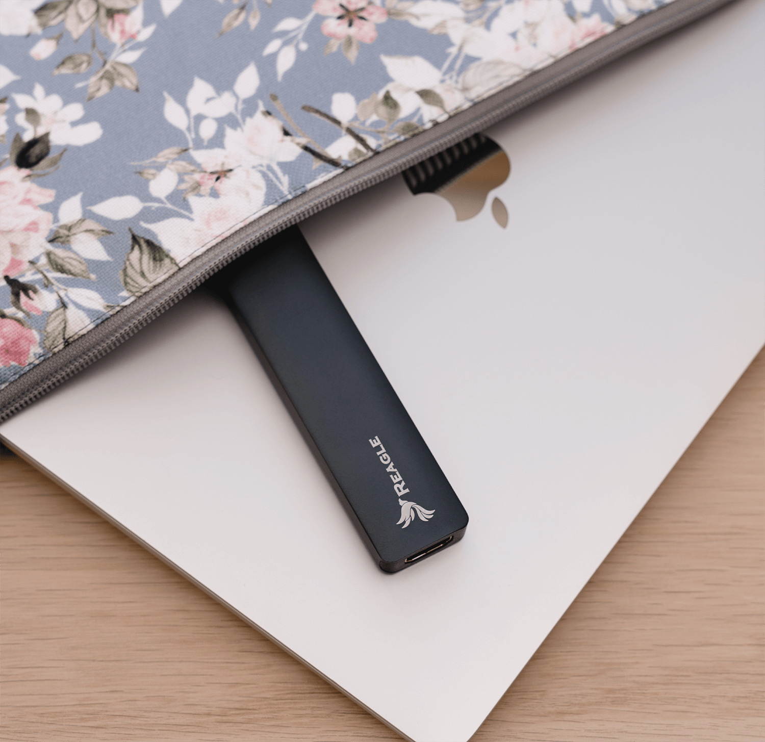 Laptop z etui, wewnątrz umieszczono ciemnoniebieski zewnętrzny dysk twardy. Etui ma kwiatowy wzór.