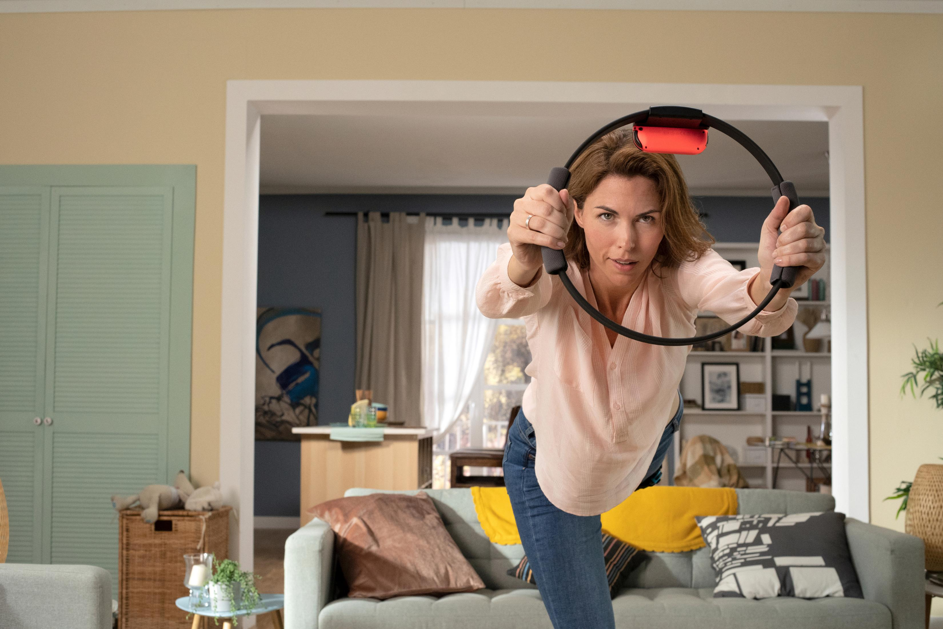 Vrouw die traint met Ring Fit. Ze is in een woonkamer. Bank, deur en raam op de achtergrond.