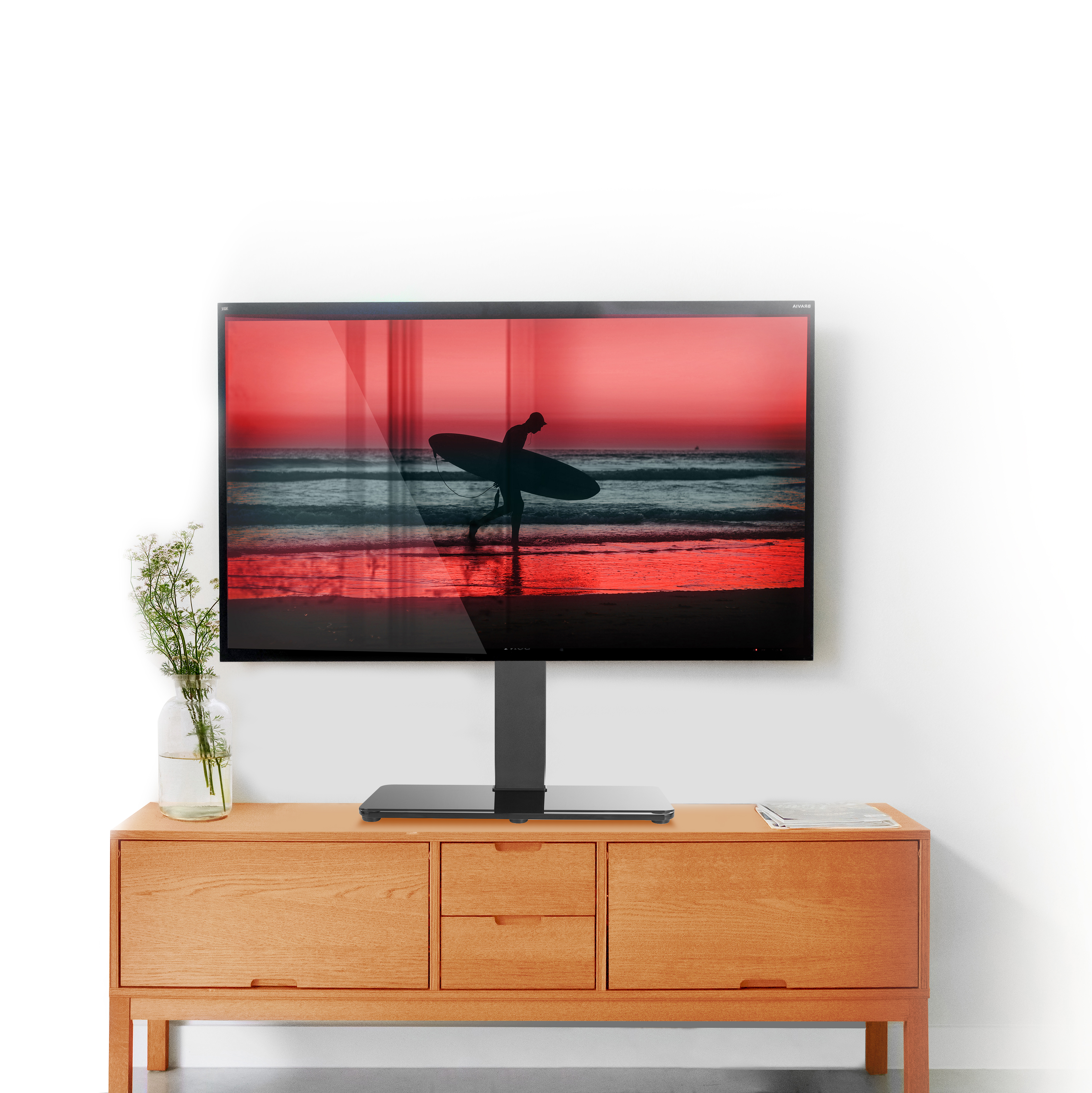 Una TV su un mobile in legno mostra una scena di spiaggia. Un vaso di fiori è a sinistra.