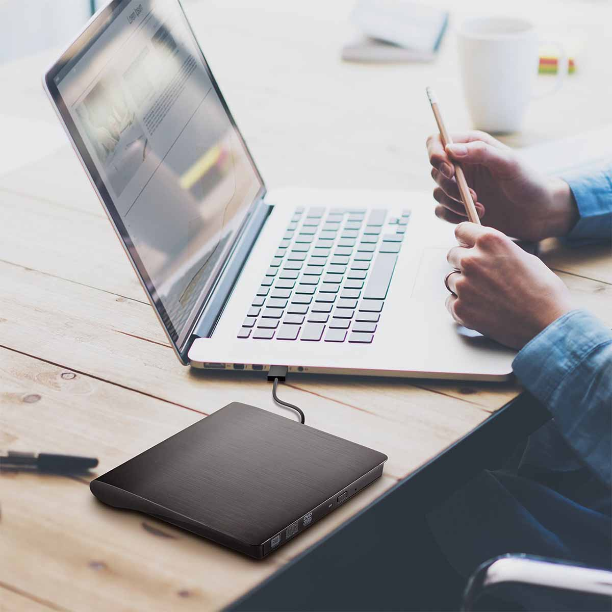 Ein Laptop mit einem DVD-Laufwerk, das angeschlossen ist. Eine Person arbeitet mit einem Bleistift.