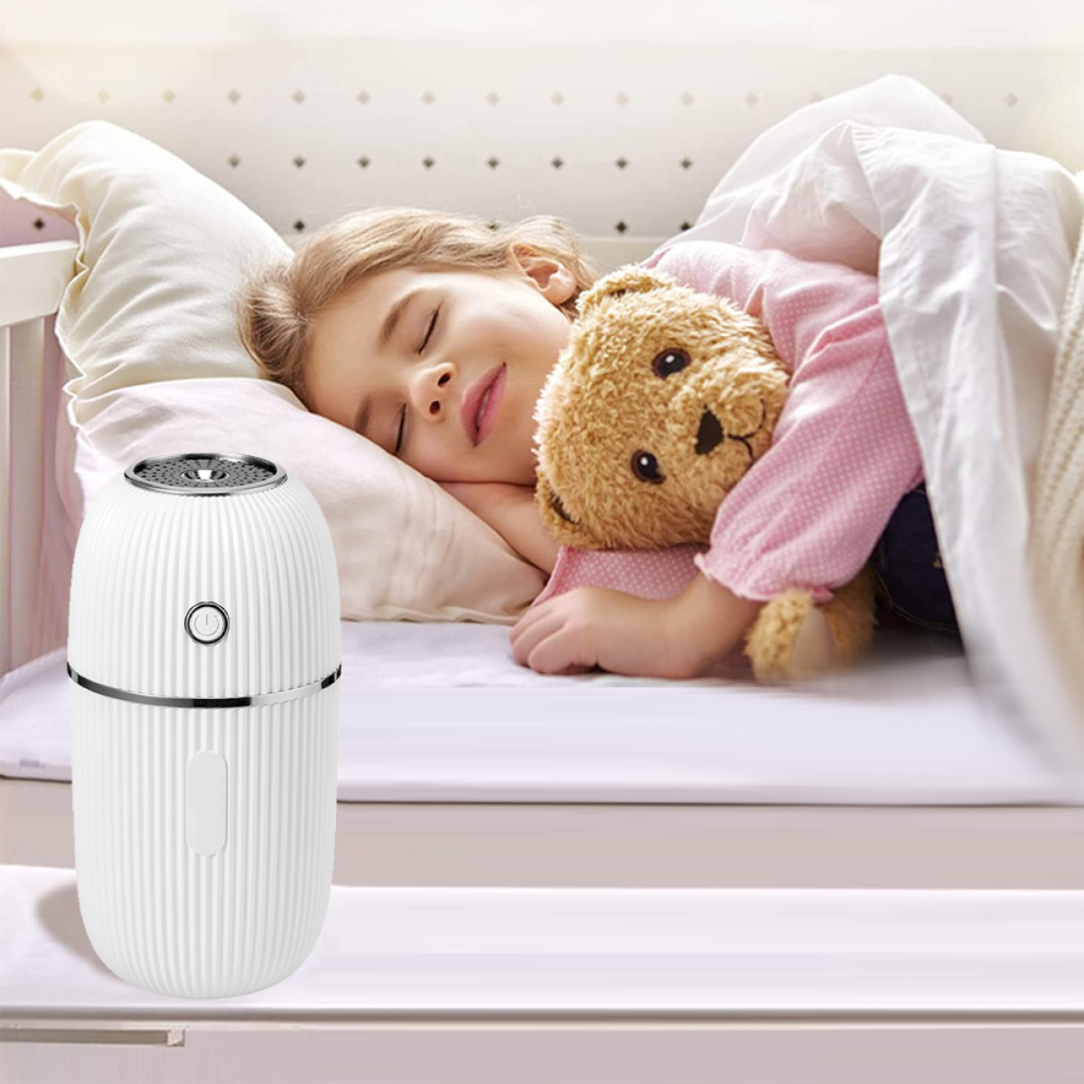 Ein Mädchen schläft in einem Kinderbett und umarmt einen Teddybären. Ein weißer Luftbefeuchter steht daneben.