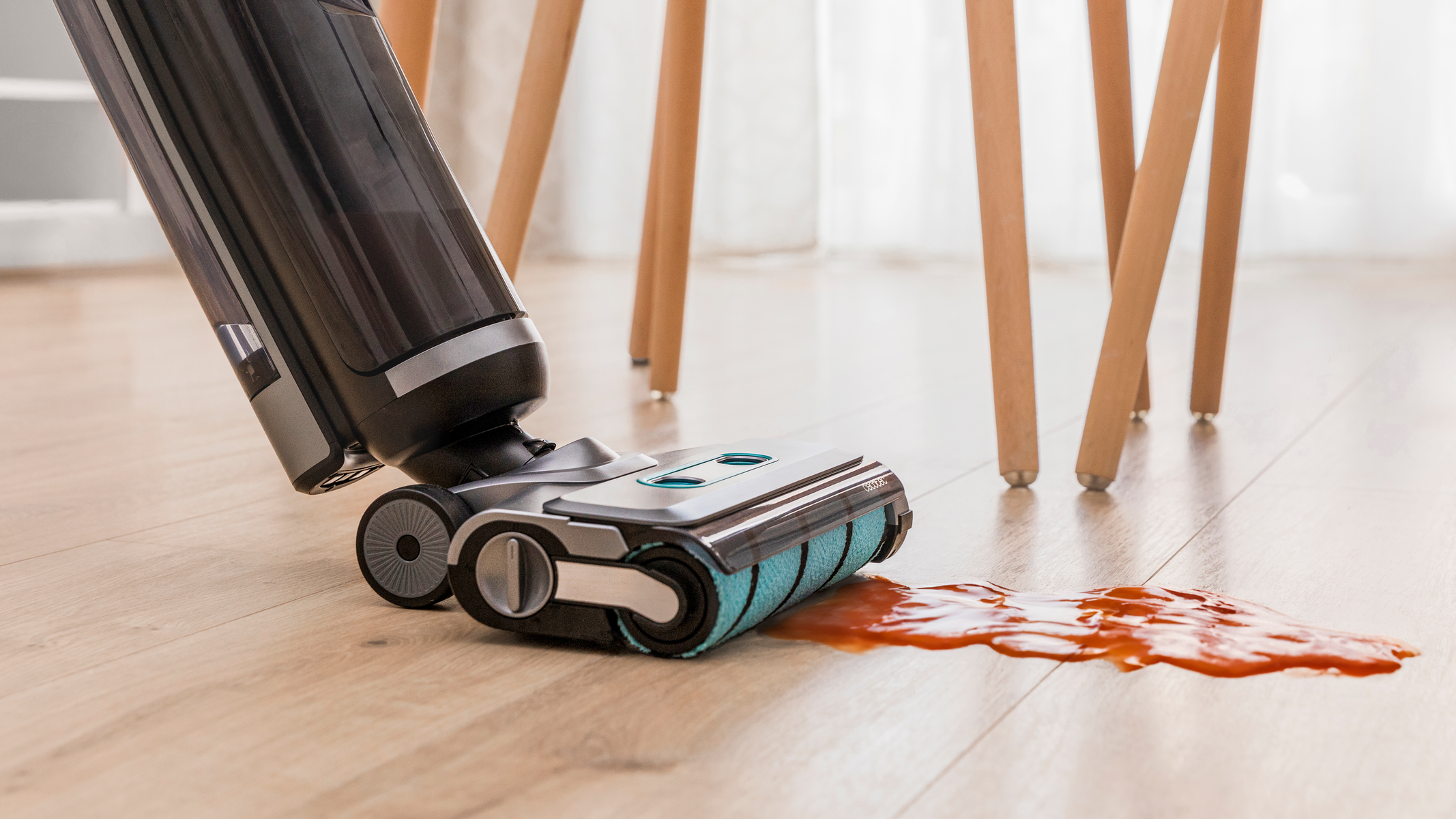 Aspirapolvere che pulisce un pavimento con una macchia rossa, con gambe di legno sullo sfondo.