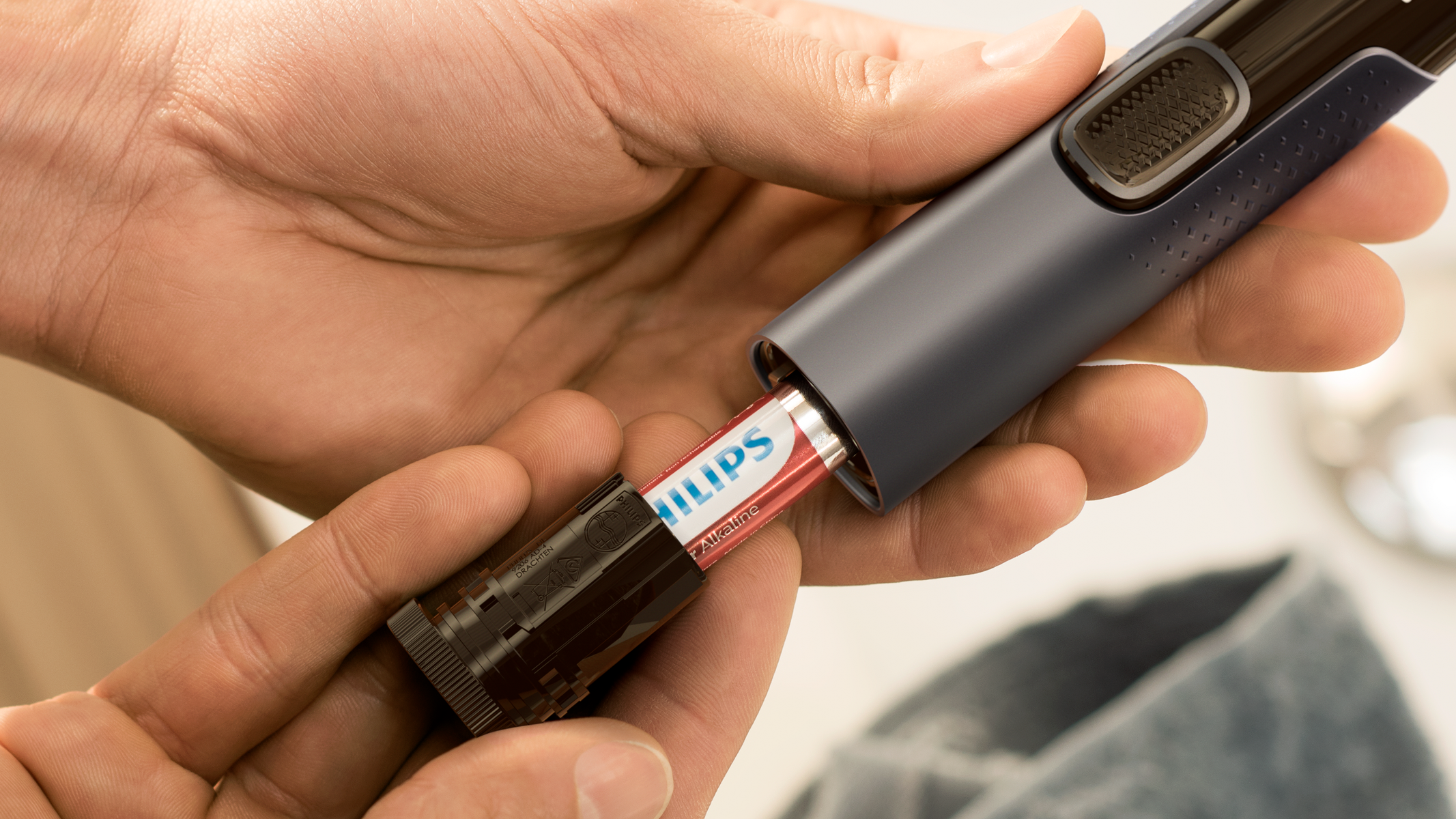 Ręce wkładające baterię do golarki. Czerwono-biała bateria jest wkładana do czarnej golarki.
