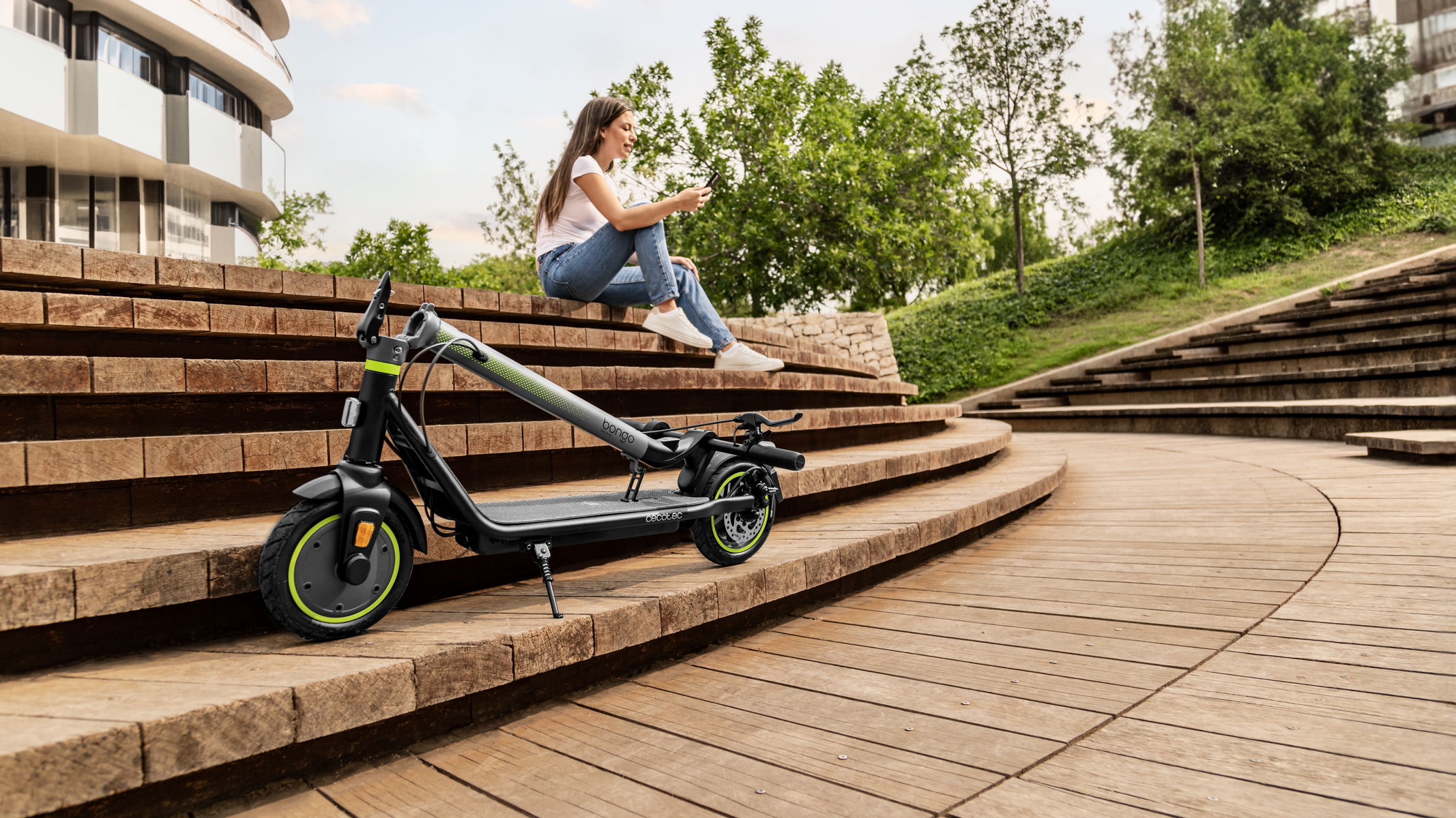 Kobieta siedzi na schodach ze skuterem, patrząc na telefon.