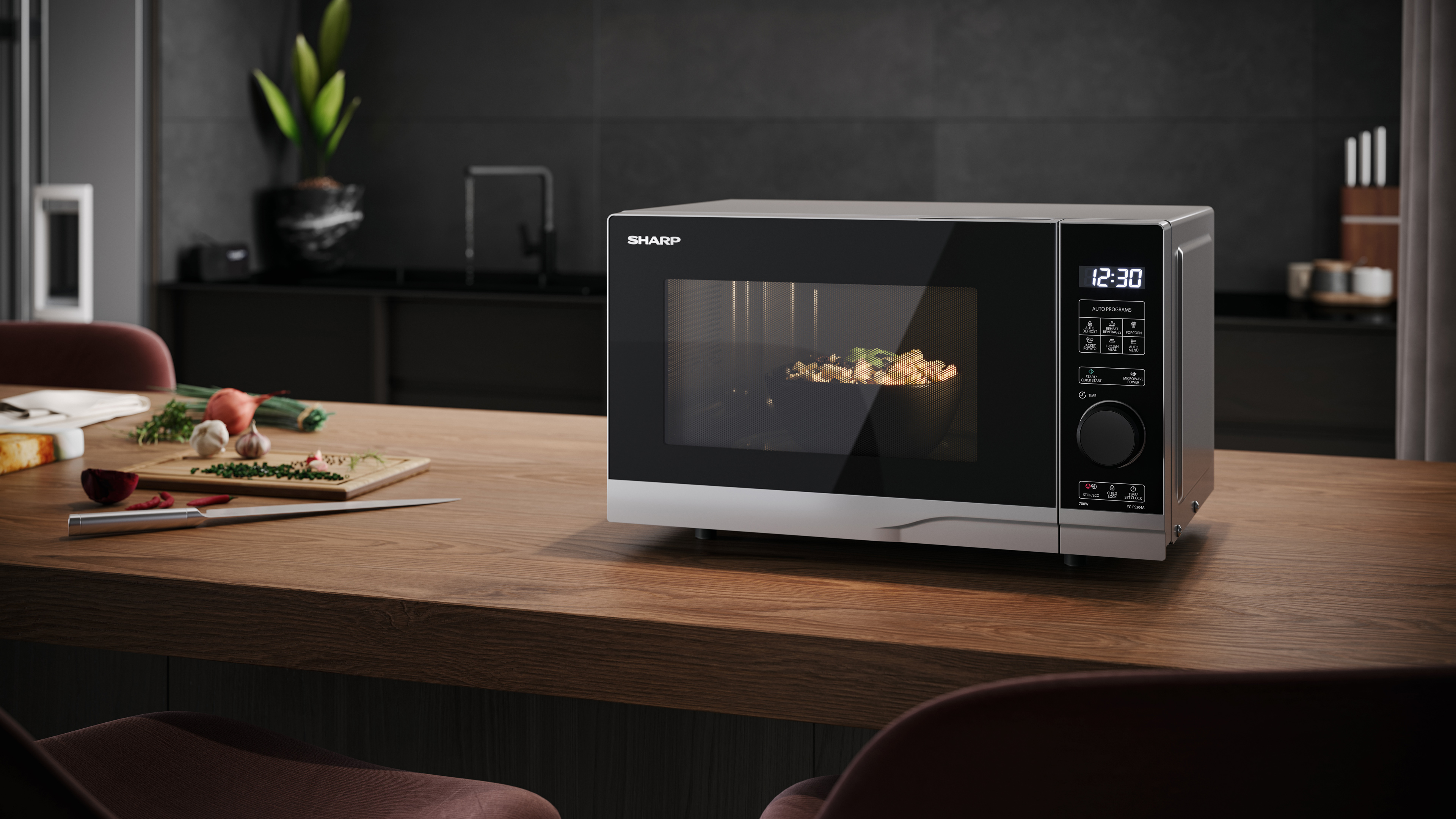 Kuchenka mikrofalowa na drewnianym stole. Makaron wewnątrz piekarnika. Kuchnia i trochę jedzenia.