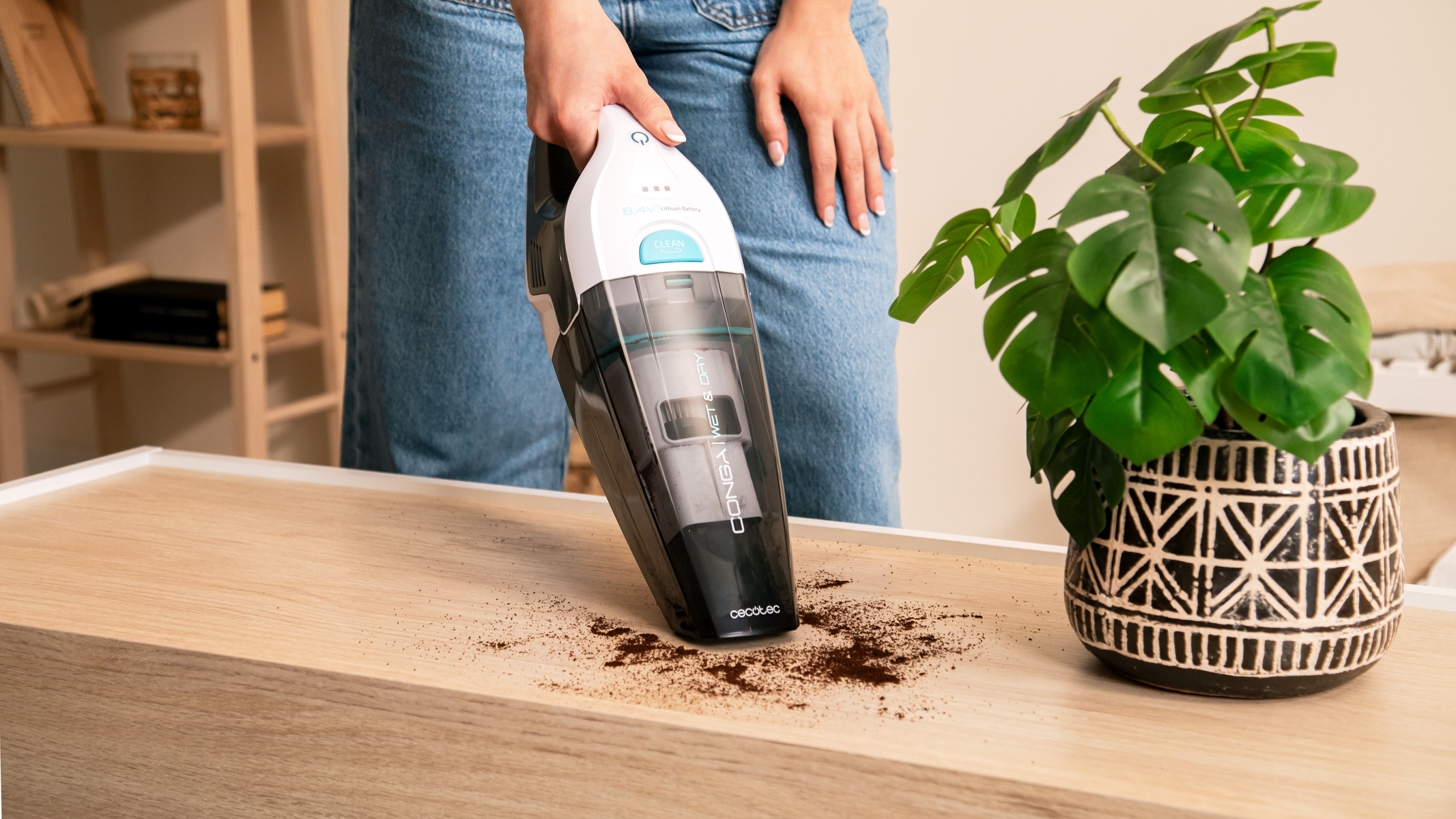 Una donna aspira fondi di caffè da una superficie di legno con un aspirapolvere bianco e nero.