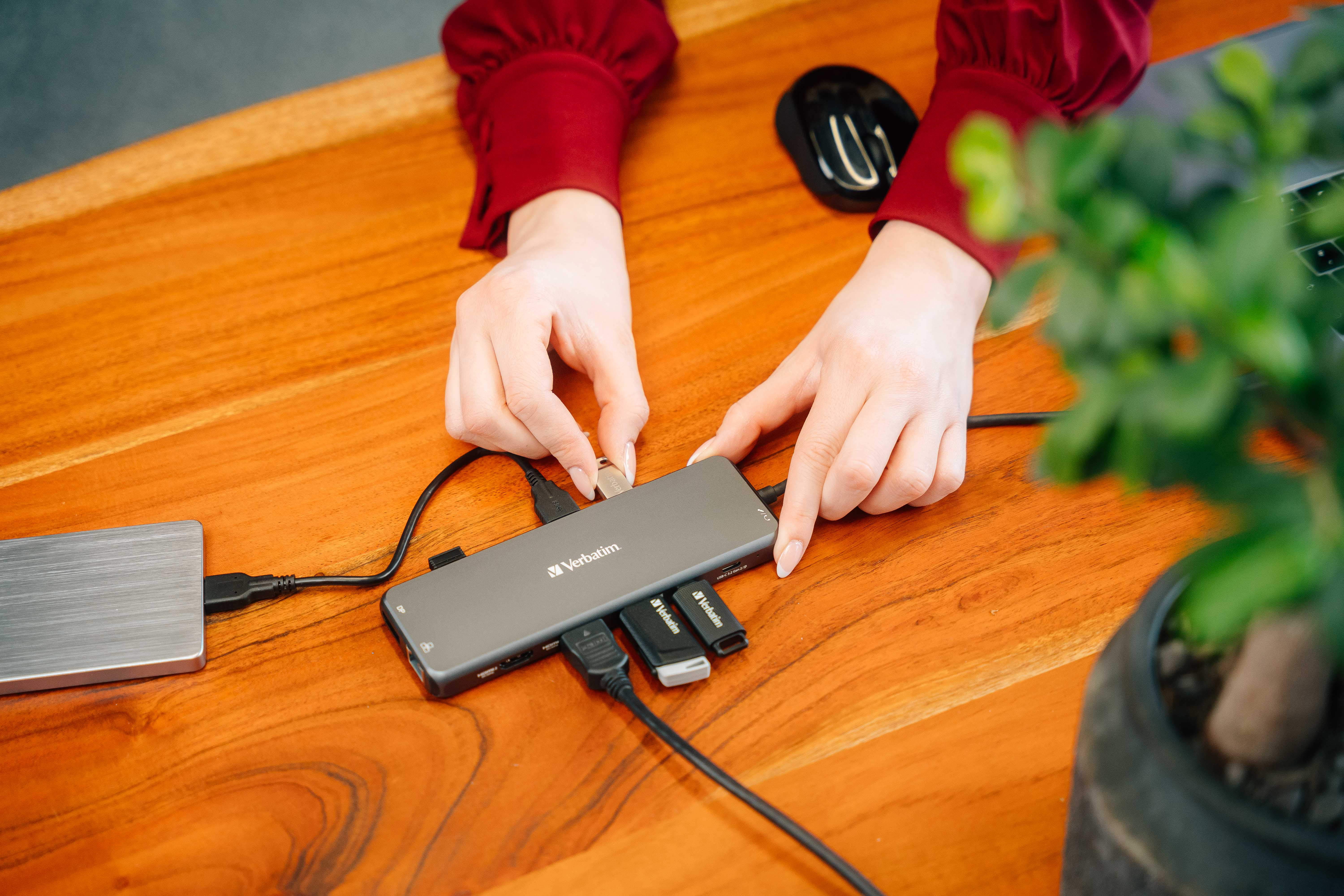 Hände, die einen USB-Hub mit anderen Geräten auf einem Holztisch verbinden. Zubehör vorhanden.