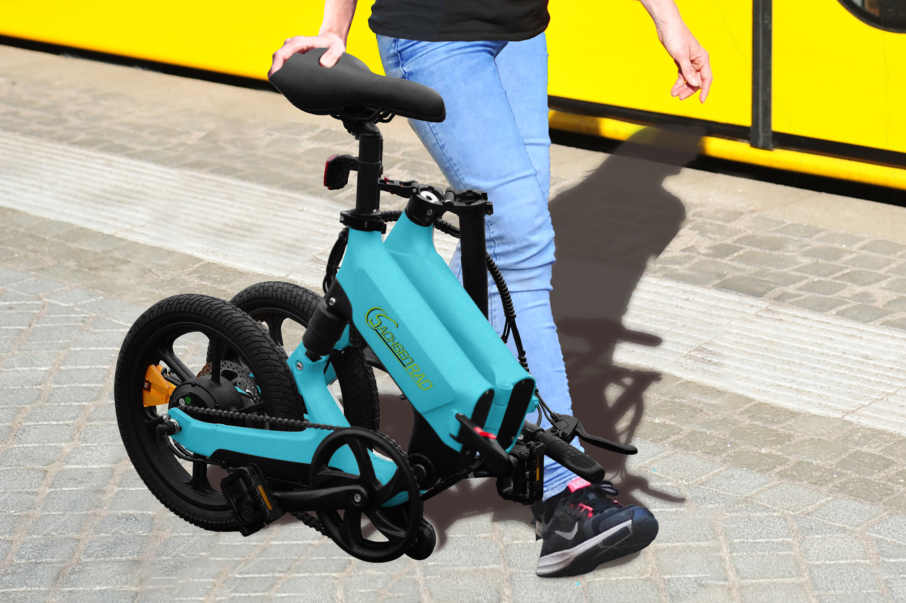 Eine Person hält ein türkisfarbenes Klapprad auf einem Bürgersteig. Das Fahrrad ist teilweise zusammengeklappt.