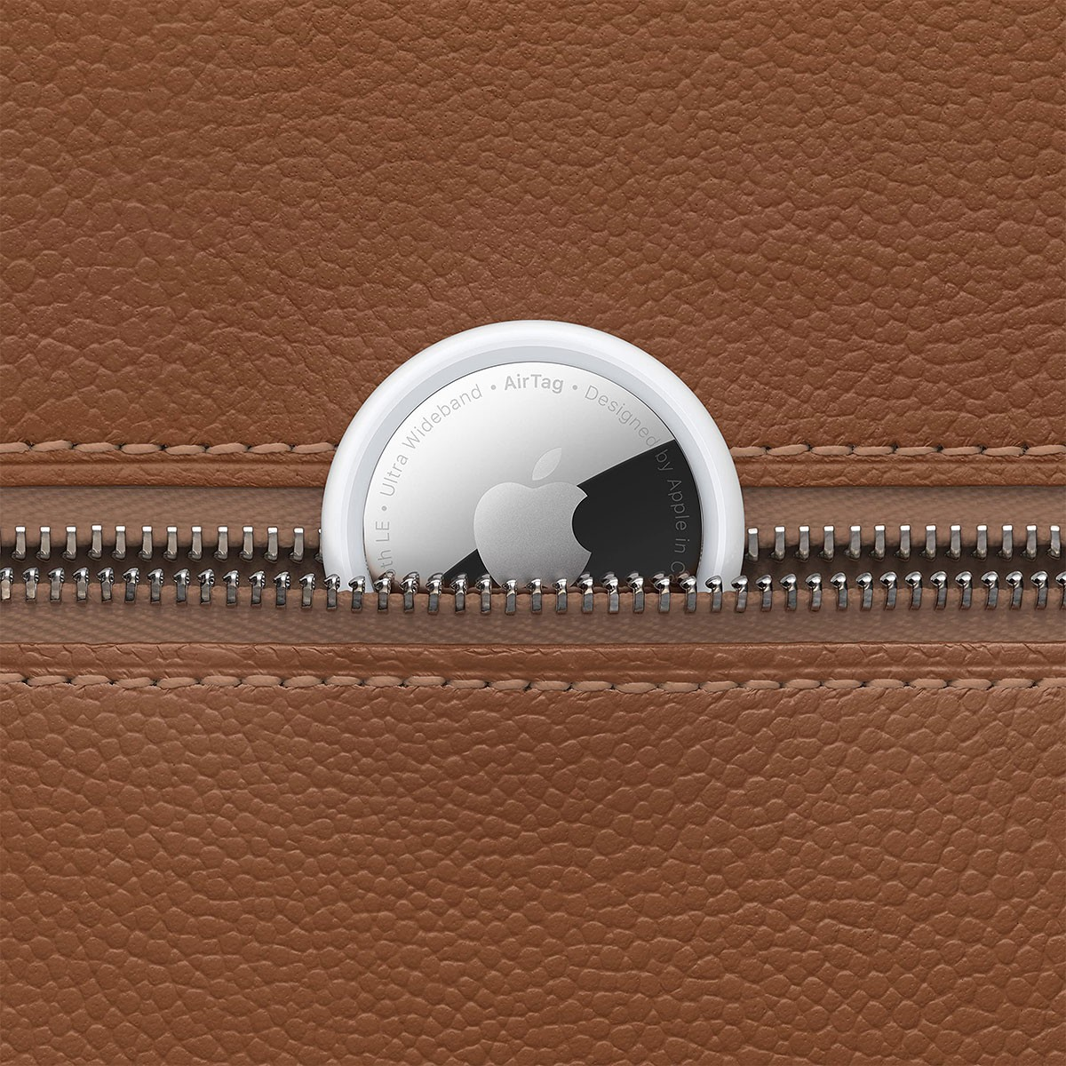 Een Apple AirTag in een bruine leren ritssluiting, half zichtbaar. De tag is wit met een zilveren Apple logo.