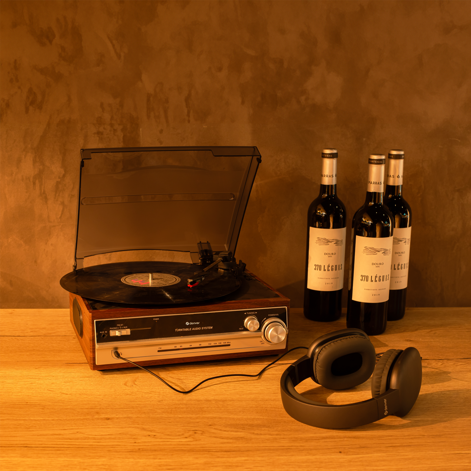 Gramofon, płyta winylowa, słuchawki, butelki wina na drewnianym stole.
