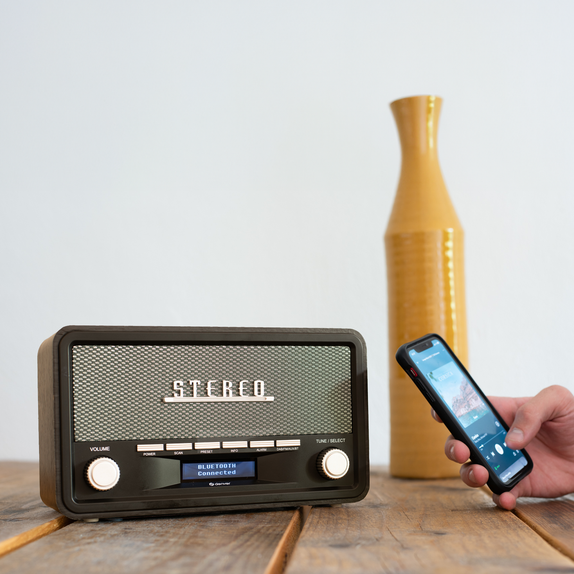 Radio stereo z telefonem odtwarzającym muzykę, z żółtym wazonem na drewnianym stole.